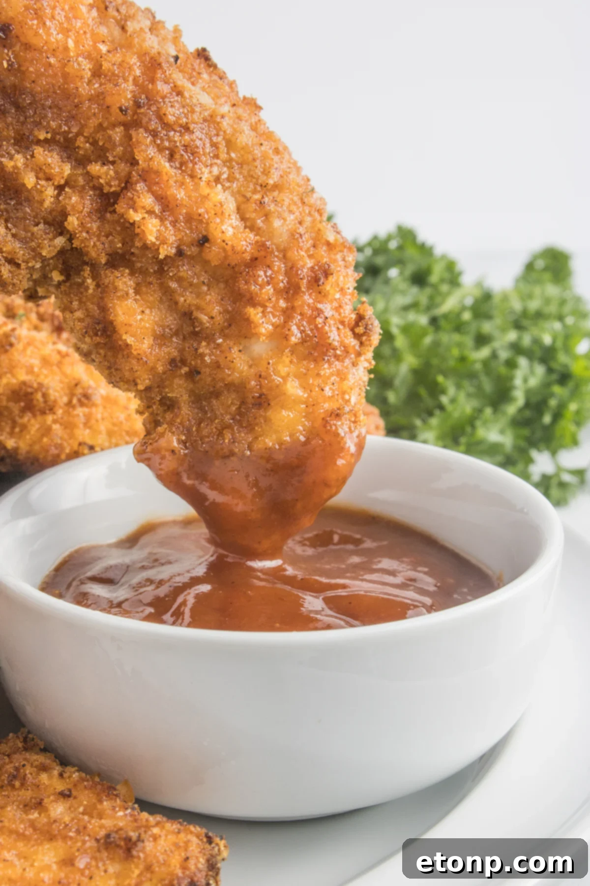Air Fryer Chicken Tender being dipped into a cup of BBQ sauce 