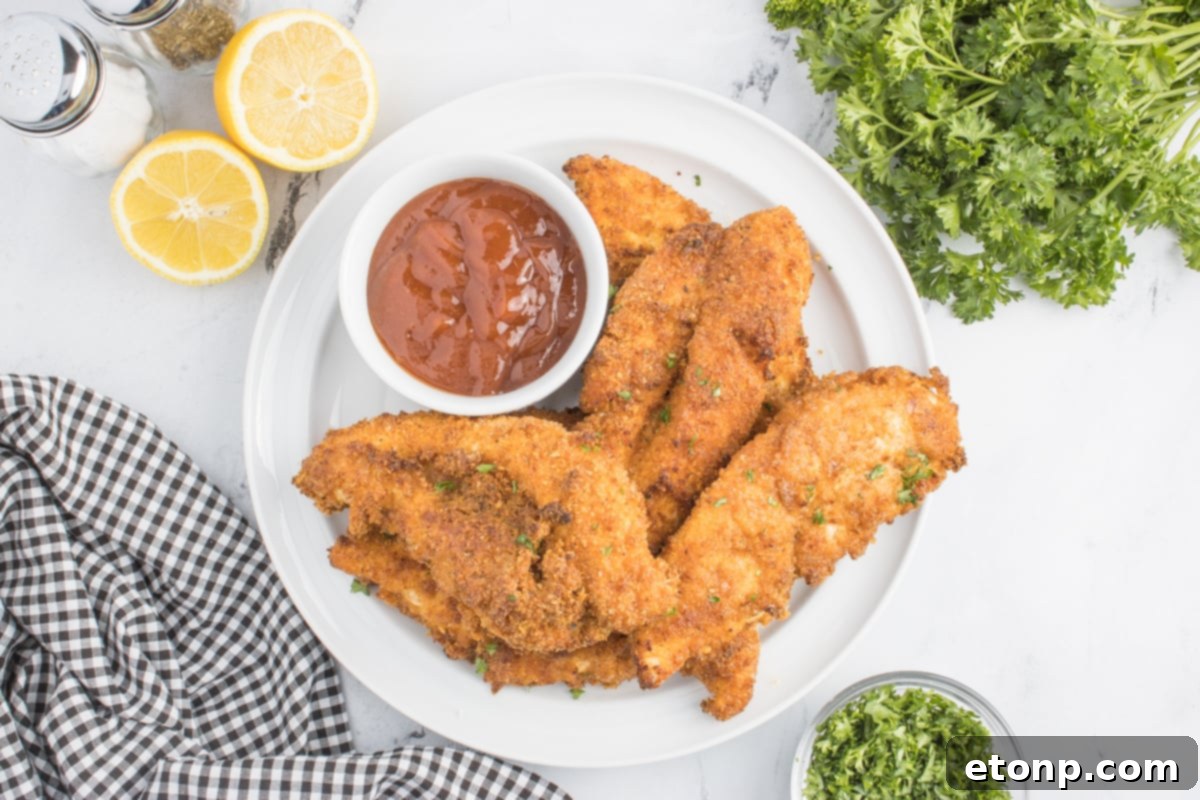 Overhead photo of the Air Fryer Chicken Tenders on a white plate with a small cup of BBQ sauce on the side 