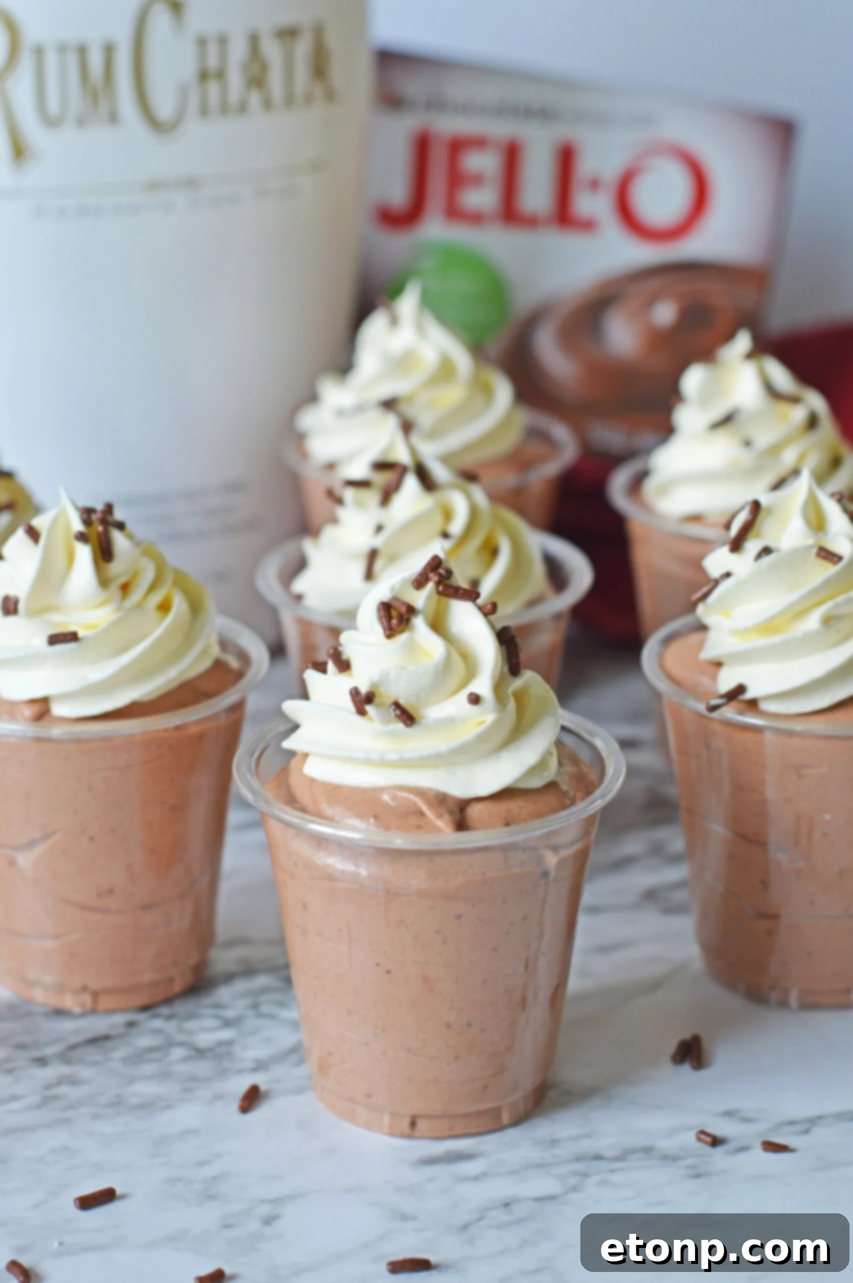 Decadent Chocolate RumChata Pudding Shots 14 Rumchata pudding shots on a marble table topped with whipped cream and sprinkles