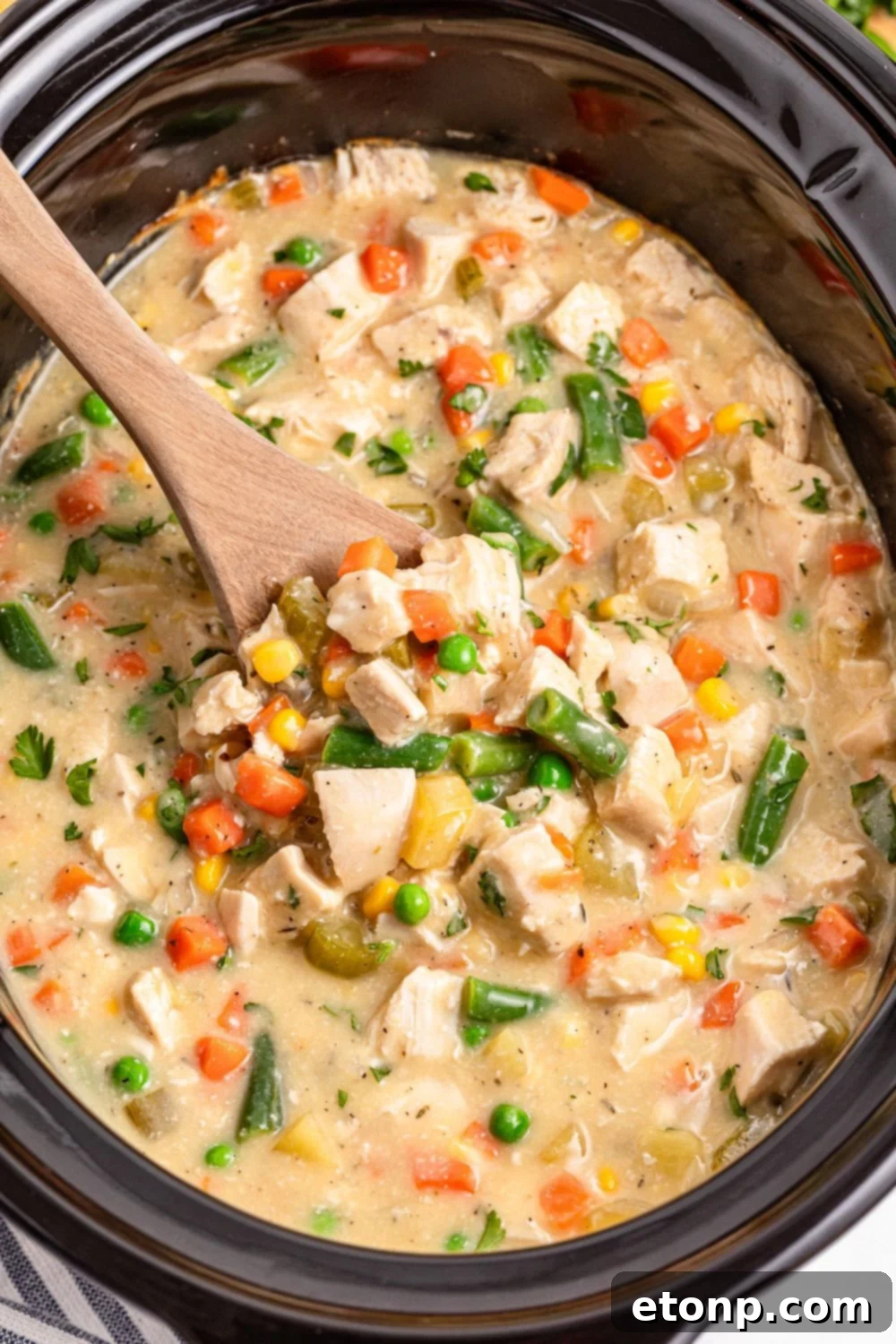 Slow Cooker Chicken Pot Pie in a slow cooker with wooden spoon scooping some out 