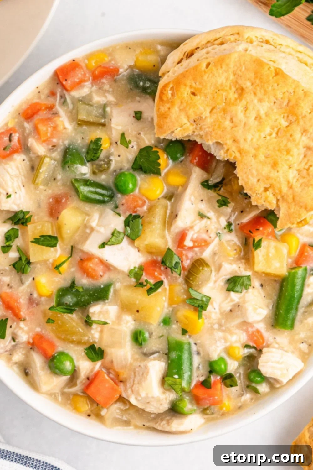 Slow Cooker Chicken Pot Pie in a bowl with some bites taken out of a biscuit on side of bowl 