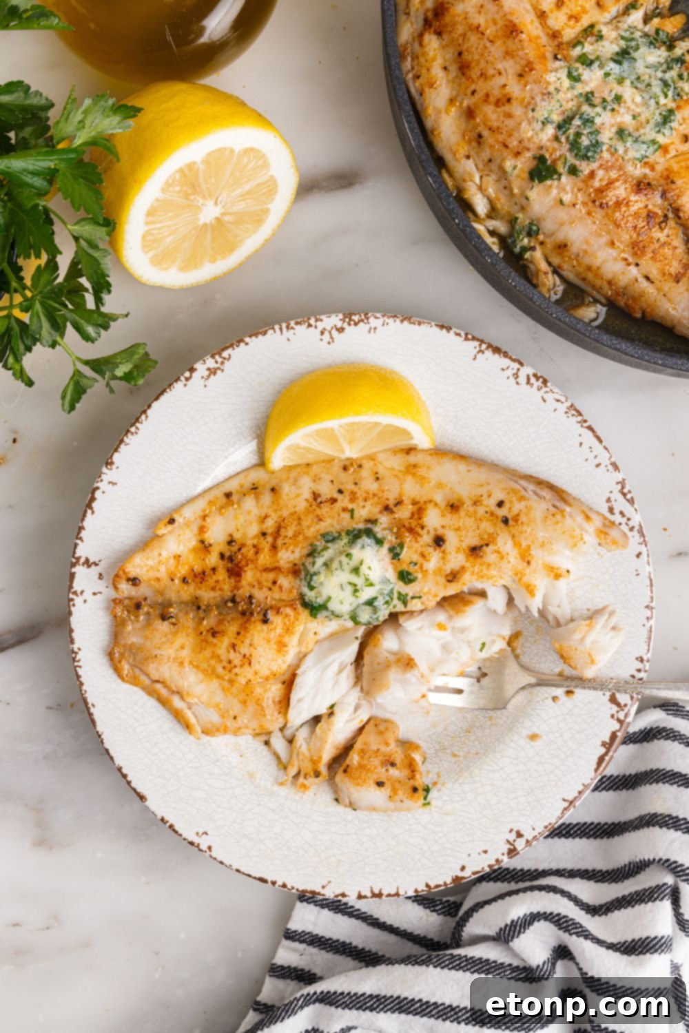 Pan Fried Tilapia on plate with pan of fish to side and lemons to showcase on side of plate