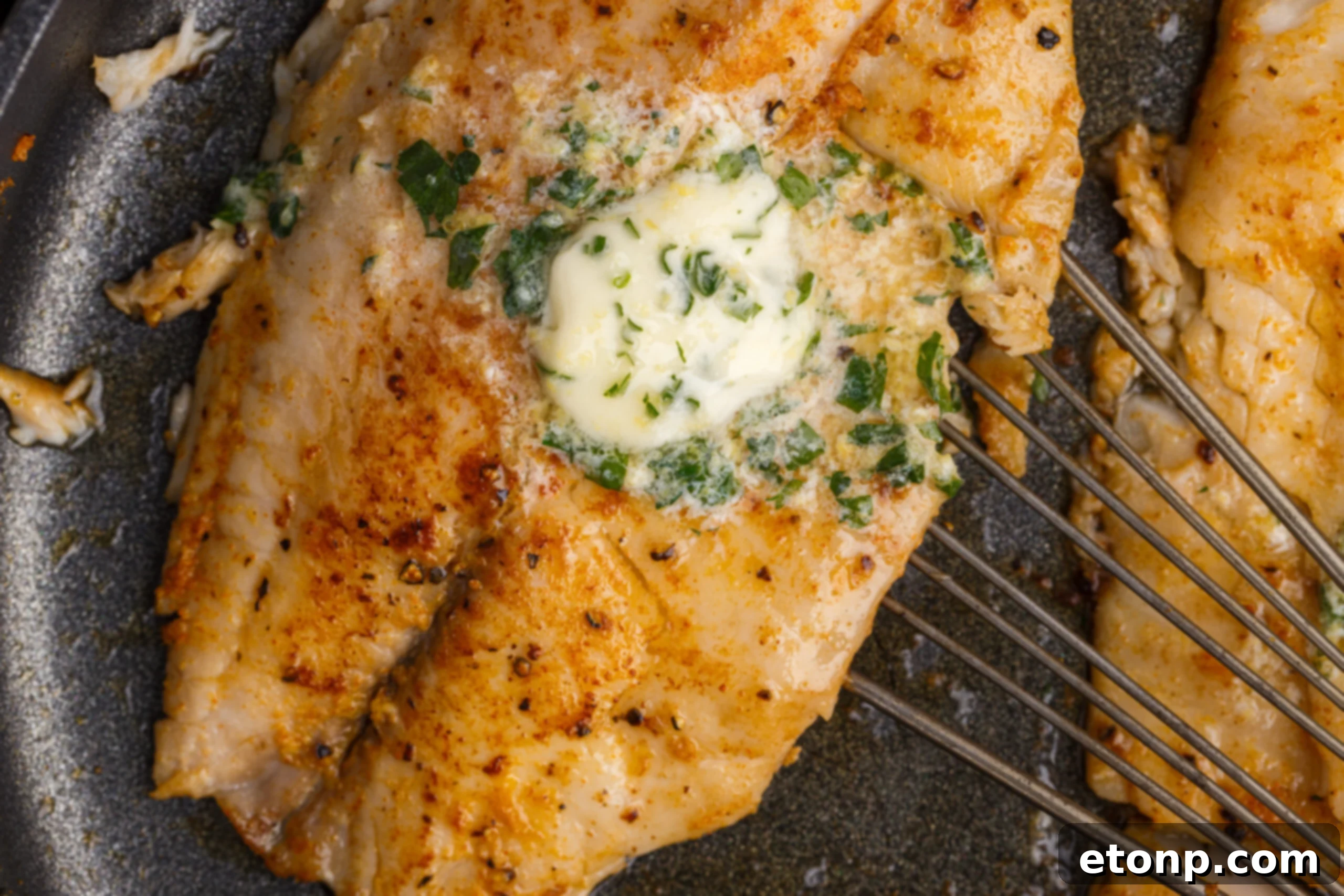 Pan Fried Tilapia in a skillet up close topped with butter