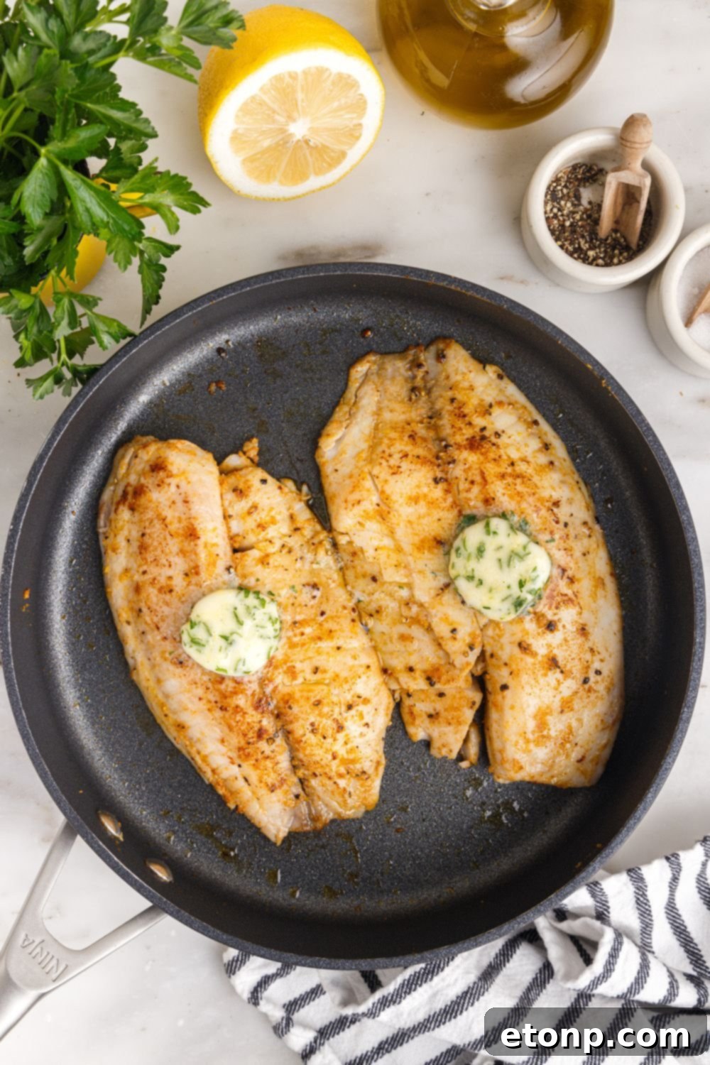 Pan Fried Tilapia in a skillet with lemon butter on top and lemon on side