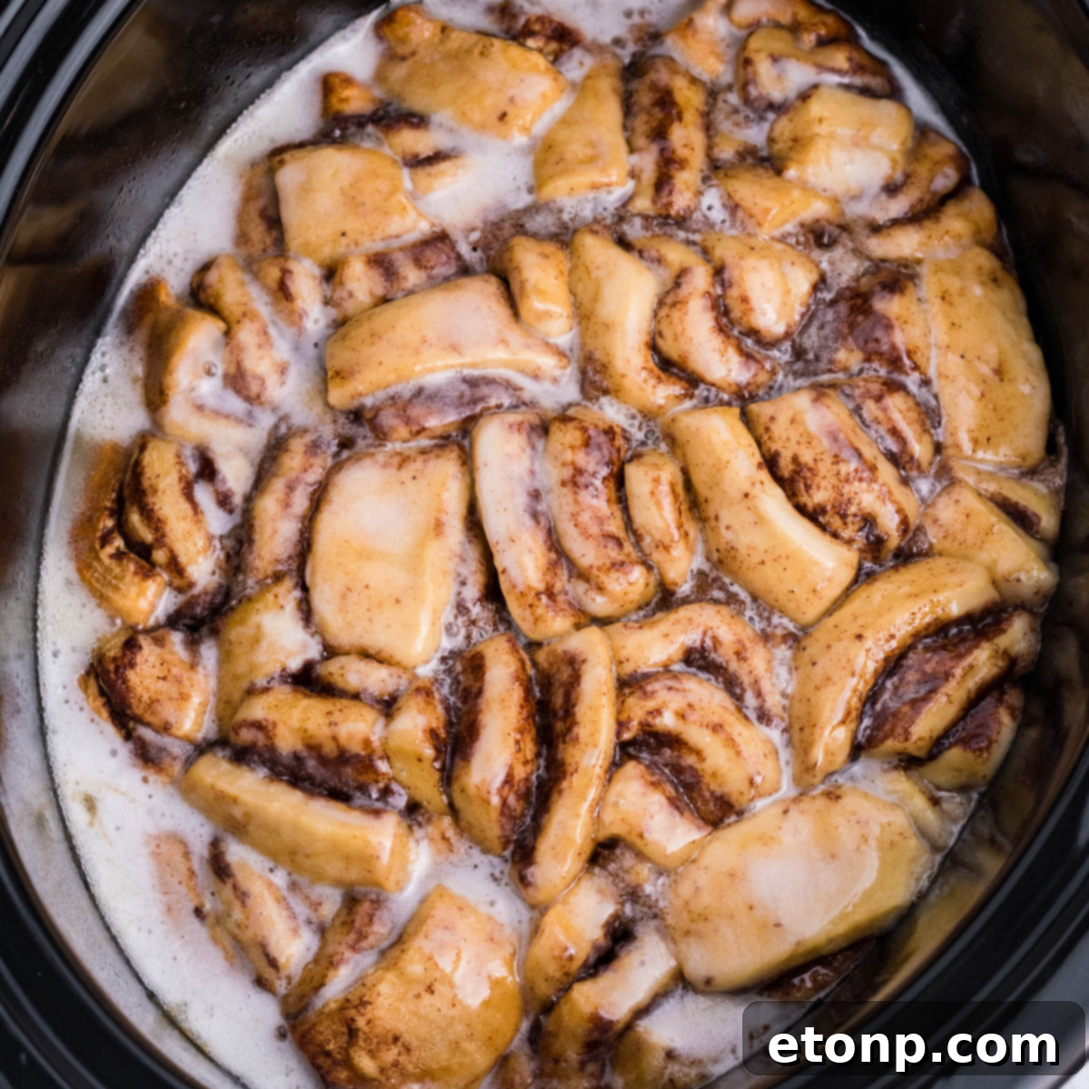 Overhead view of Crock Pot Cinnamon Roll Casserole in a black crock pot insert, garnished with icing.