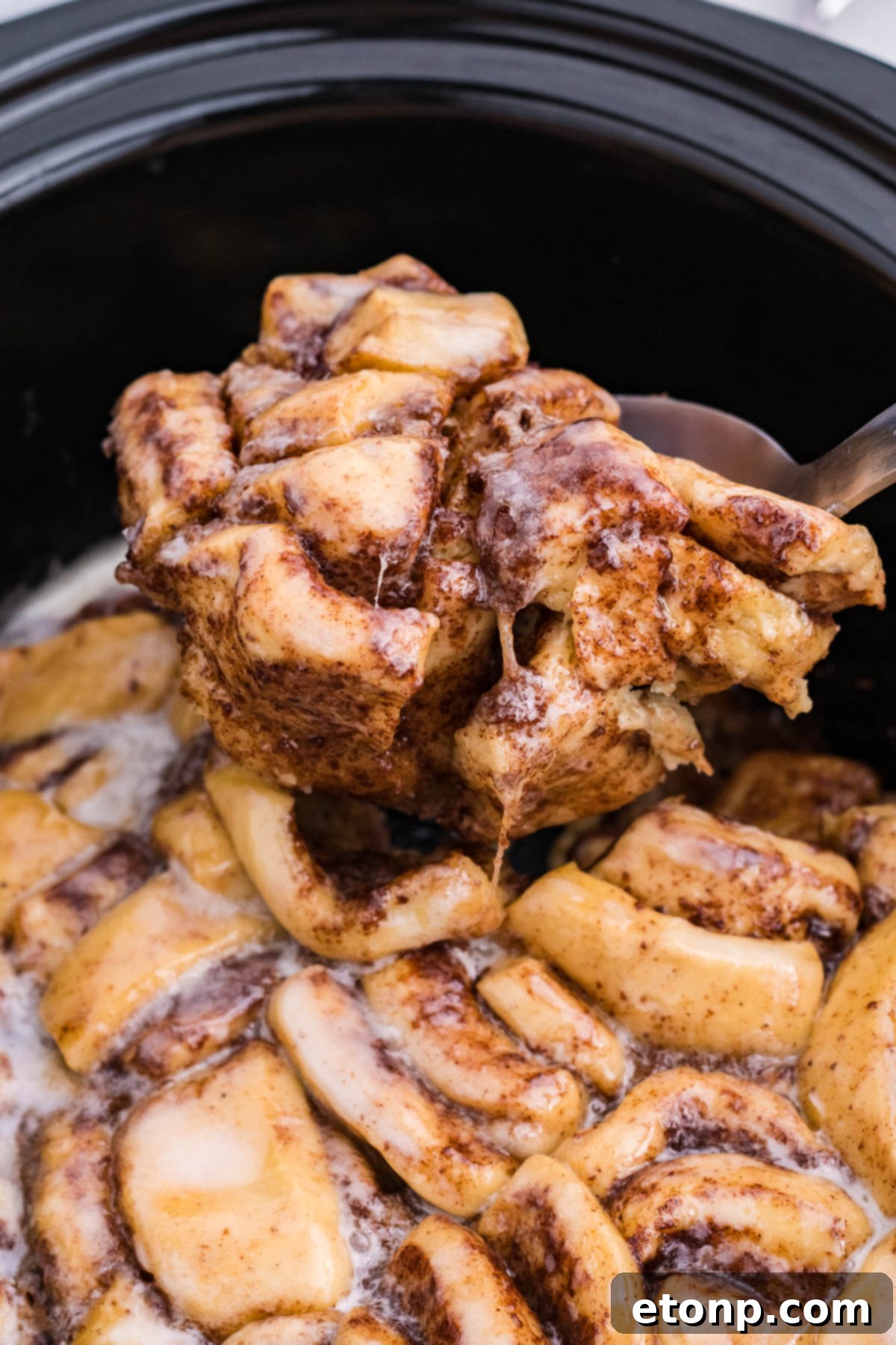 Close up view of the warm Crock Pot Cinnamon Roll Casserole being served using a large silver spoon.
