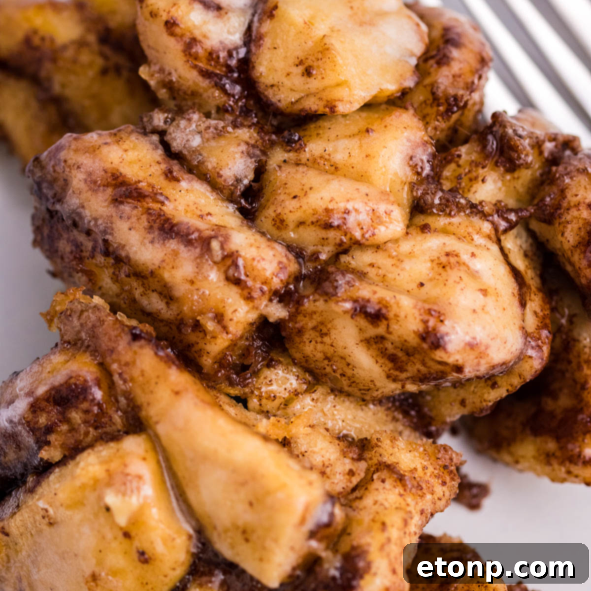 Up close view of the delicious cinnamon sugar topping on a piece of Crock Pot Cinnamon Roll Casserole on a white plate.