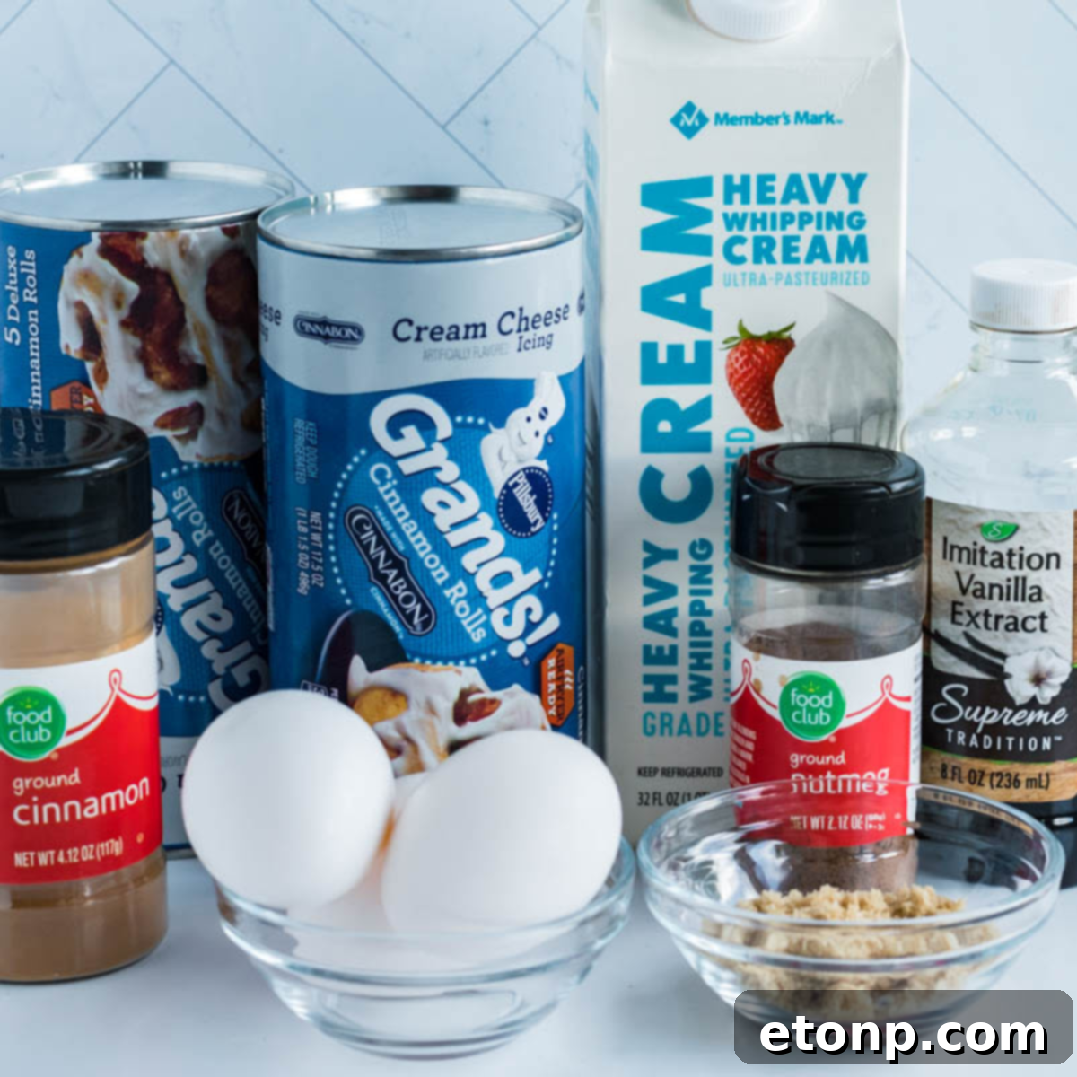 All ingredients laid out neatly needed to make Crock Pot Cinnamon Roll Casserole: cinnamon rolls, eggs, cream, brown sugar, vanilla, cinnamon, and nutmeg.