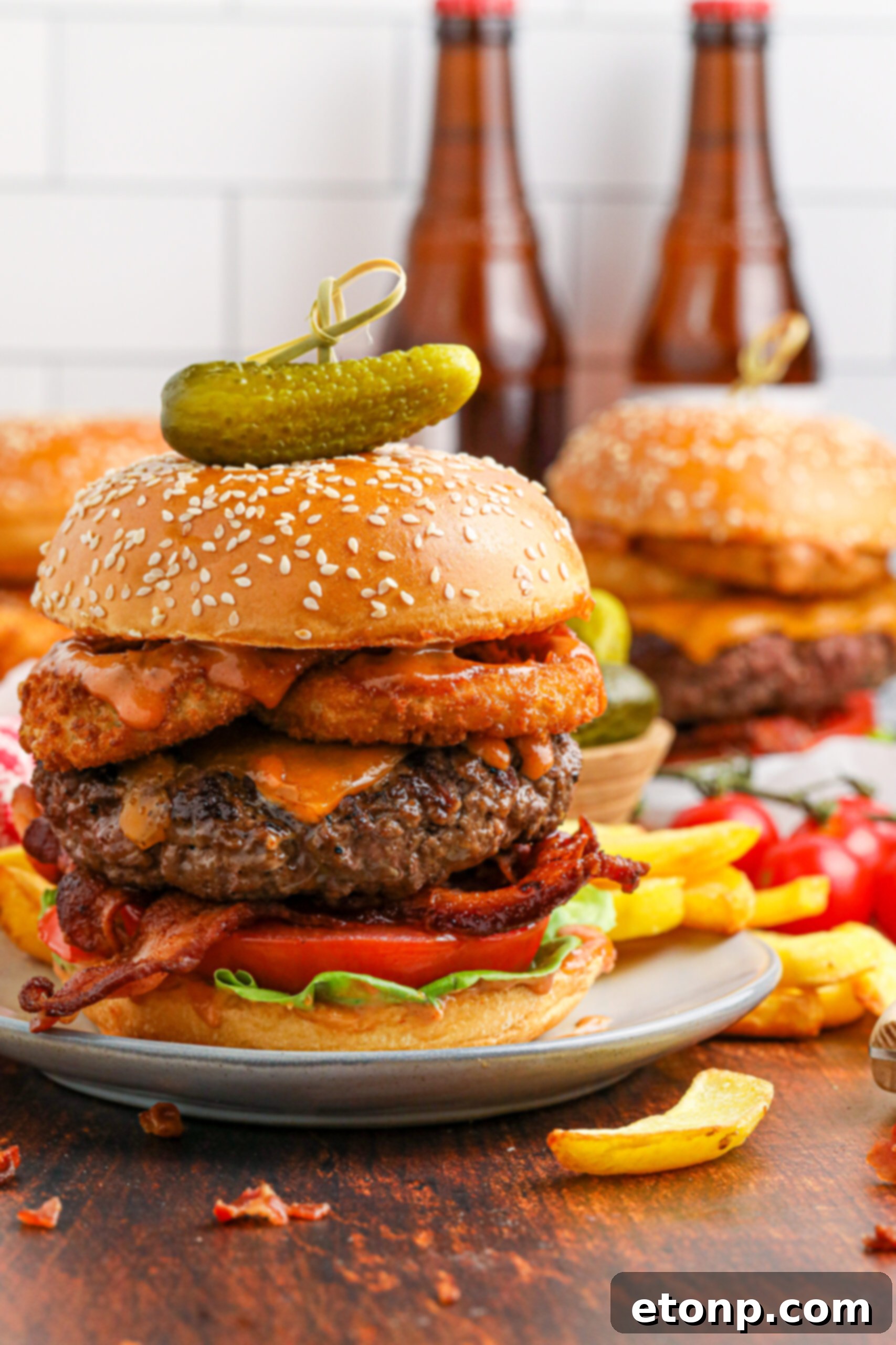 up close side view of the Cowboy Burger on a white plate that is fully loaded with toppings with a small pickle on top
