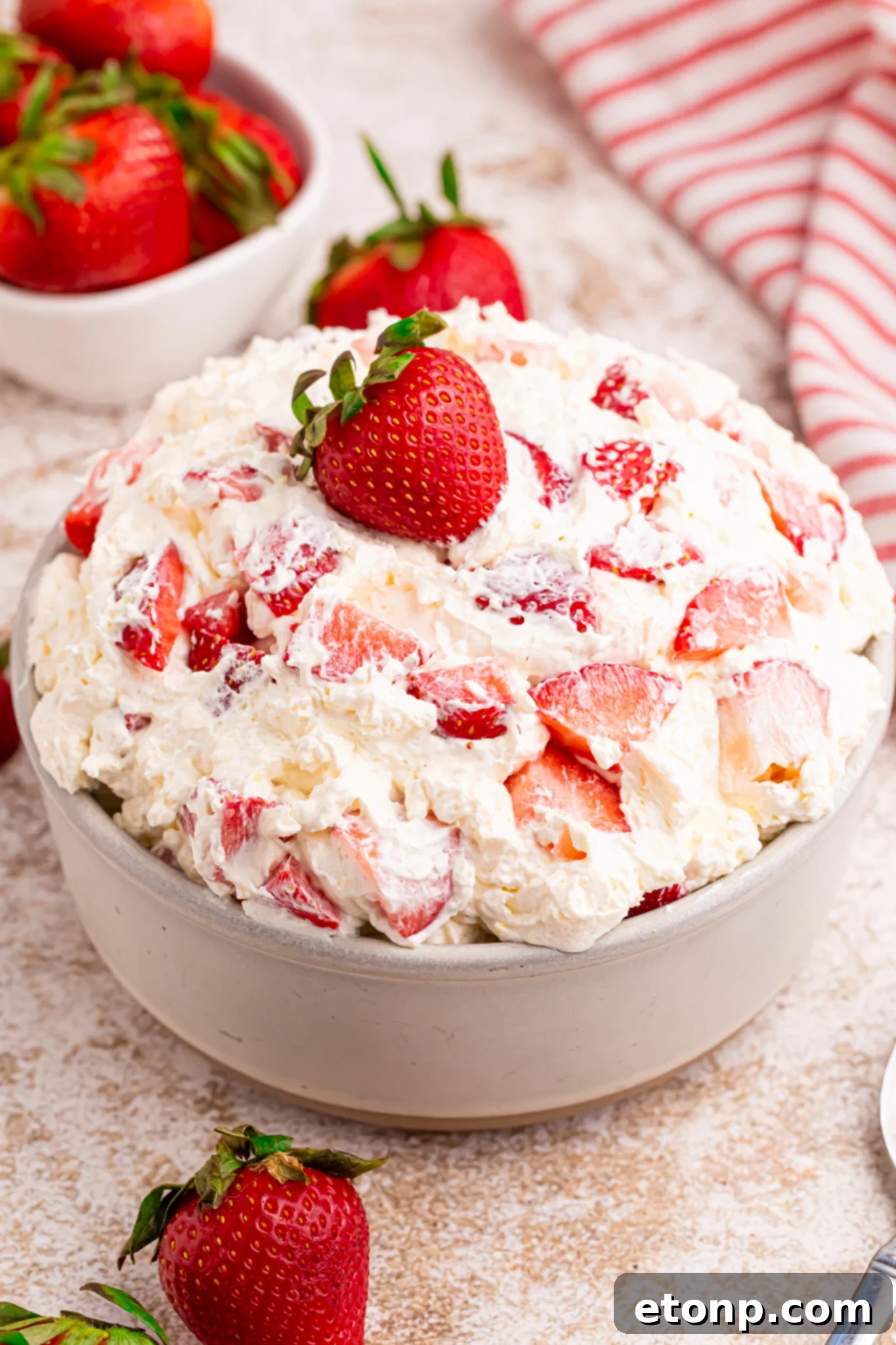 Overhead view of the strawberry cheesecake salad in a white bowl with a fresh strawberry on top. 