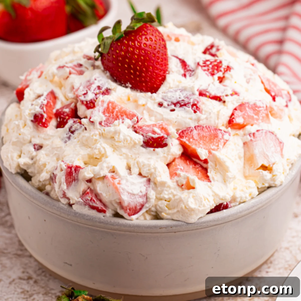 Side view of the strawberry cheesecake salad in a white bowl with a fresh strawberry on top. 
