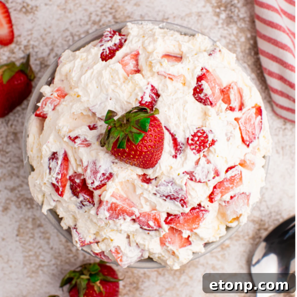 Overhead view of the strawberry cheesecake salad in a white bowl with a fresh strawberry on top. 