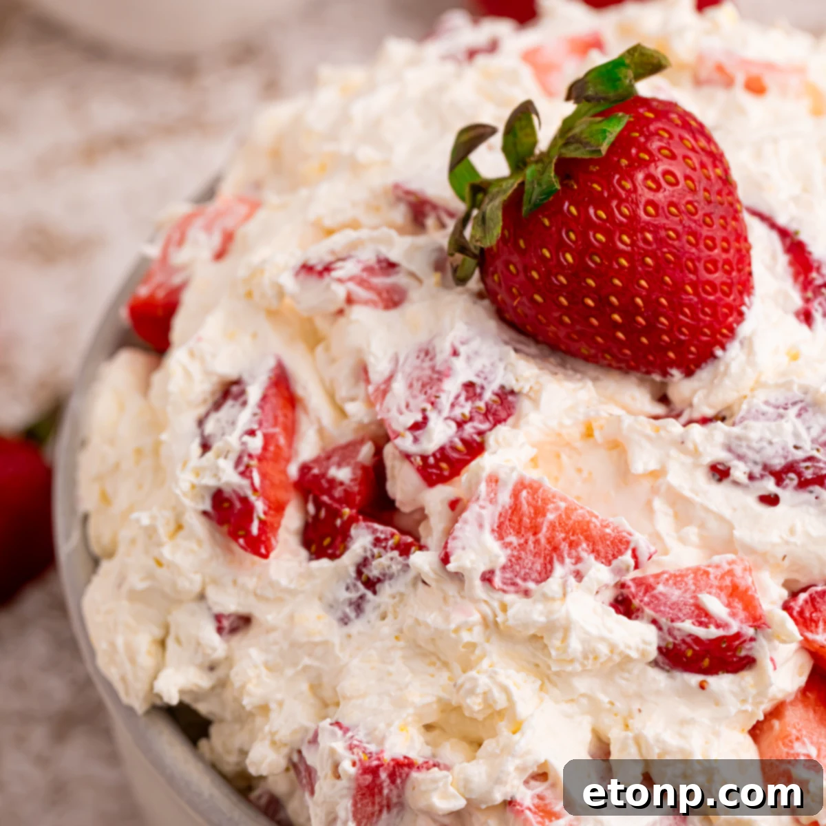 Close up view of the strawberry cheesecake salad in a white bowl with a fresh strawberry on top. 