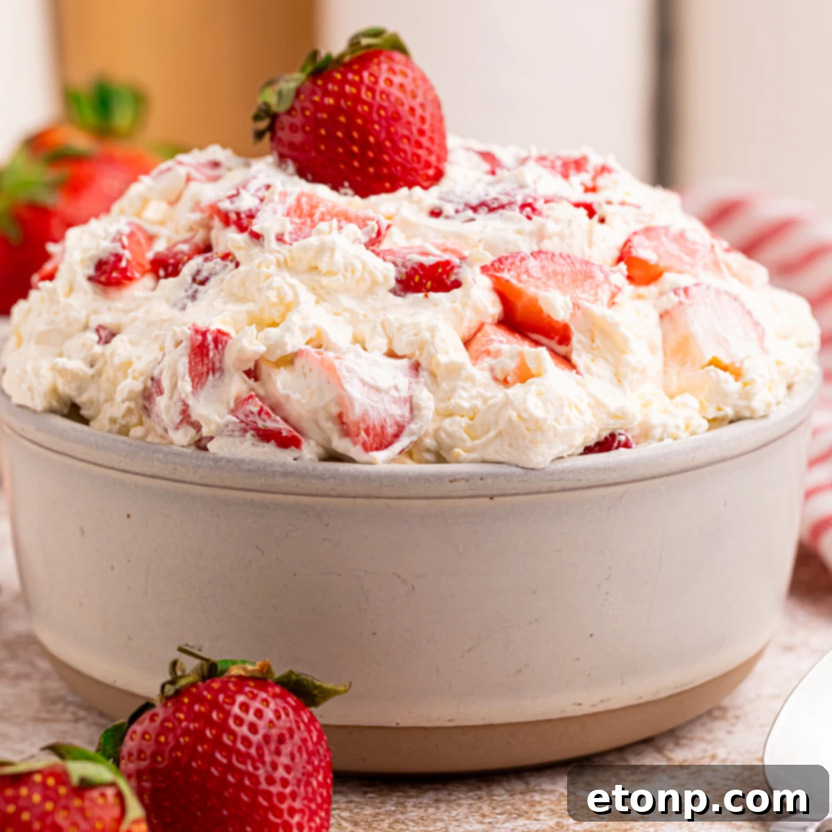 Side view of the strawberry cheesecake salad in a white bowl with a fresh strawberry on top. 