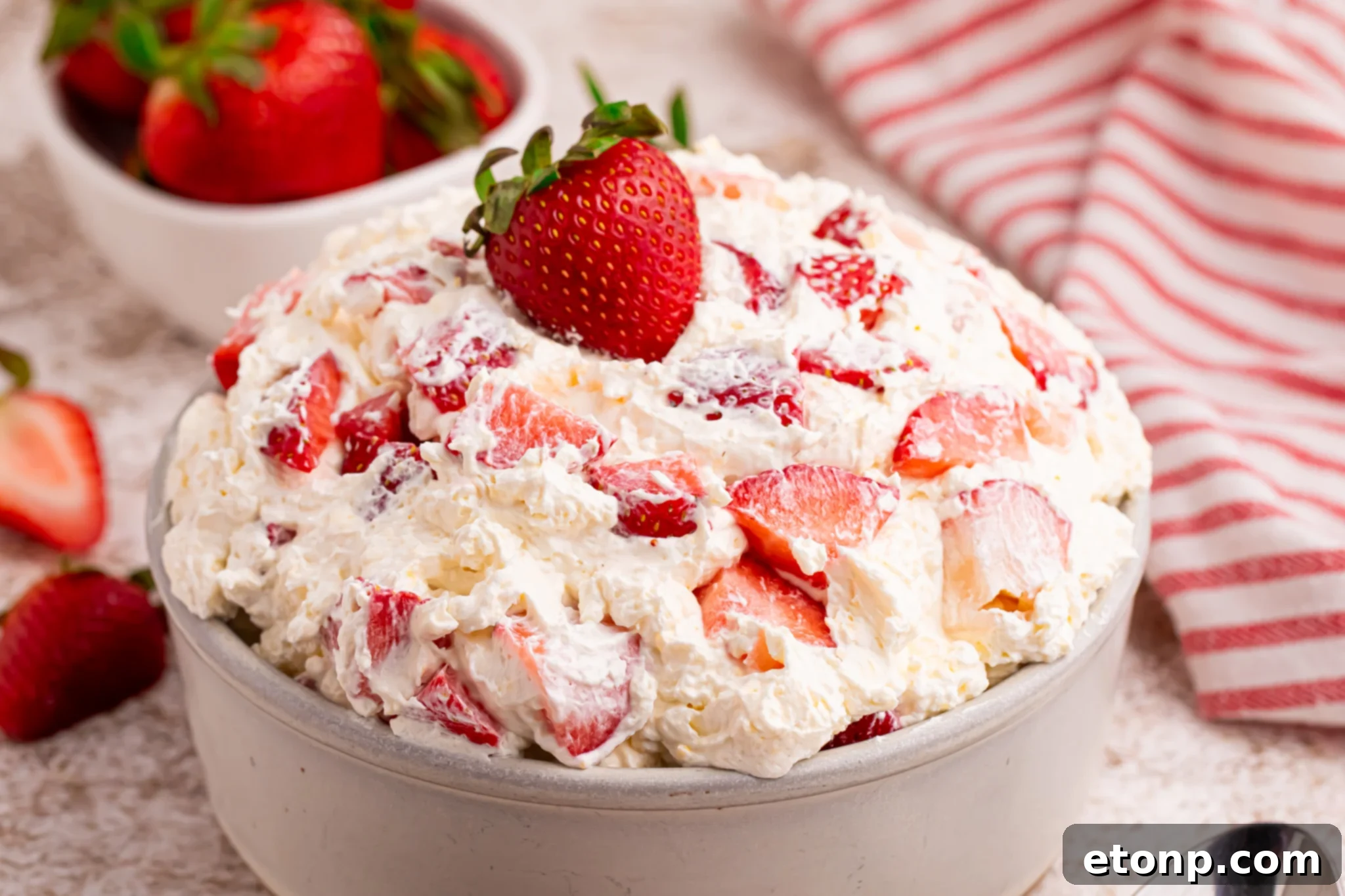 side shot of the strawberry cheesecake salad in a white bowl with a fresh strawberry on top. 