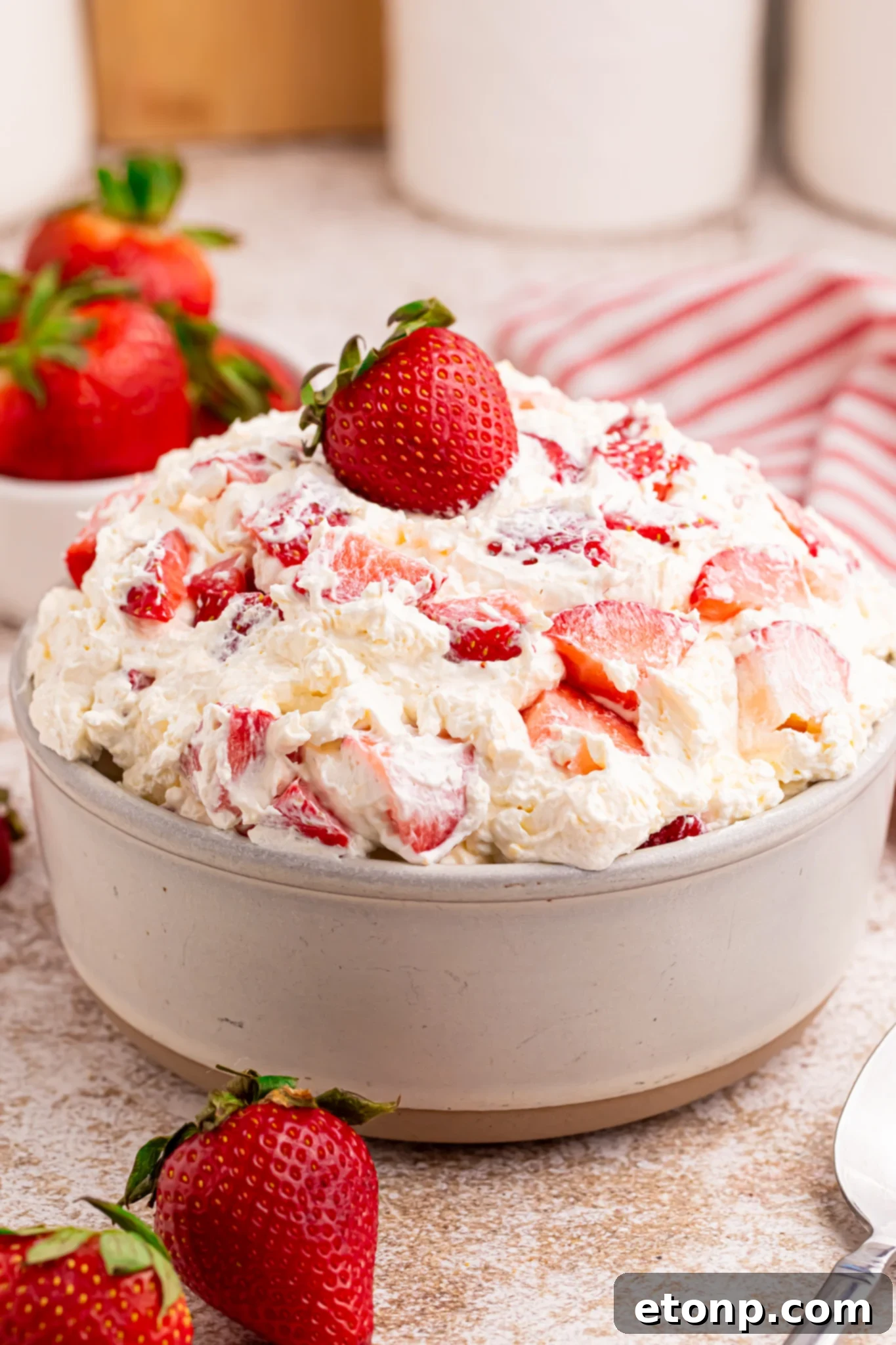 side shot of Overhead view of the strawberry cheesecake salad in a white bowl with a fresh strawberry on top. 