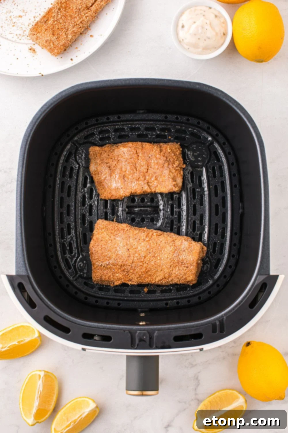 Close-up of raw, breaded fish fillets arranged in a single layer within the air fryer basket, ensuring even cooking.
