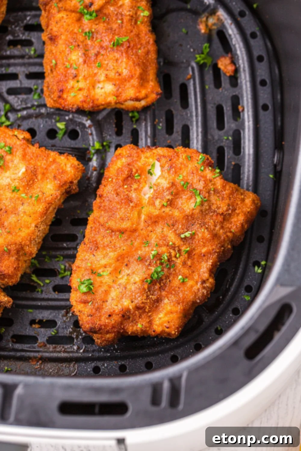 Golden-brown, crispy air fryer fish fillets cooking inside the air fryer basket, indicating they are almost done.