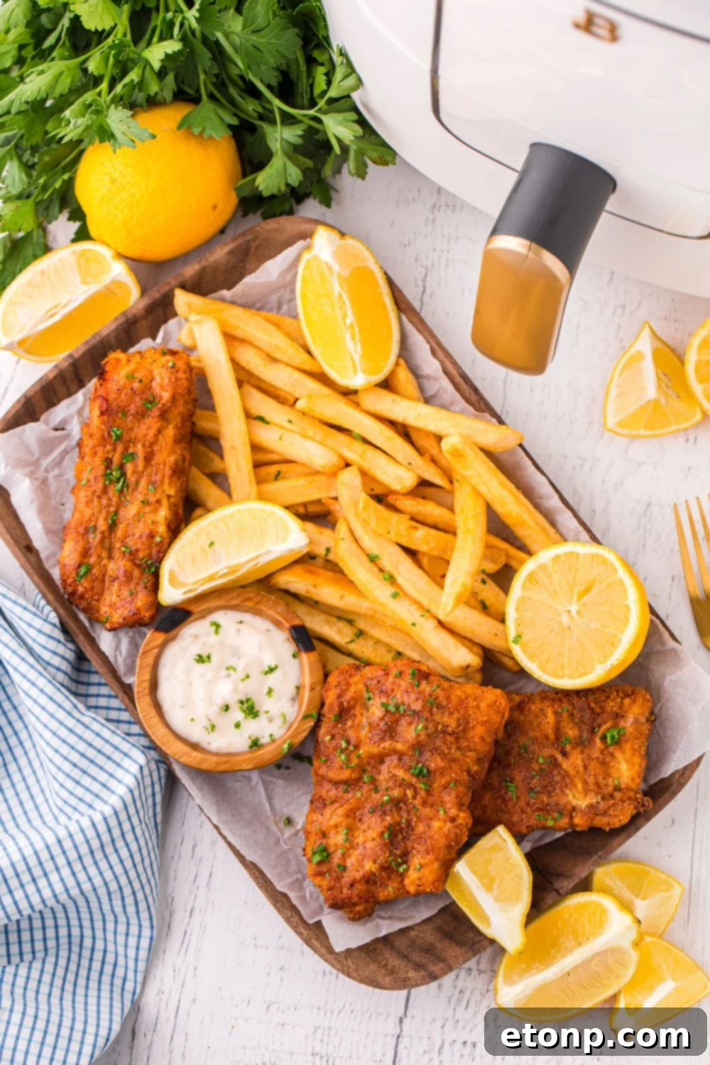 Overhead shot of Air Fryer Fish and Chips arranged on a serving tray, accompanied by lemon slices, fresh parsley, and the air fryer unit positioned to the side, highlighting a complete culinary scene.