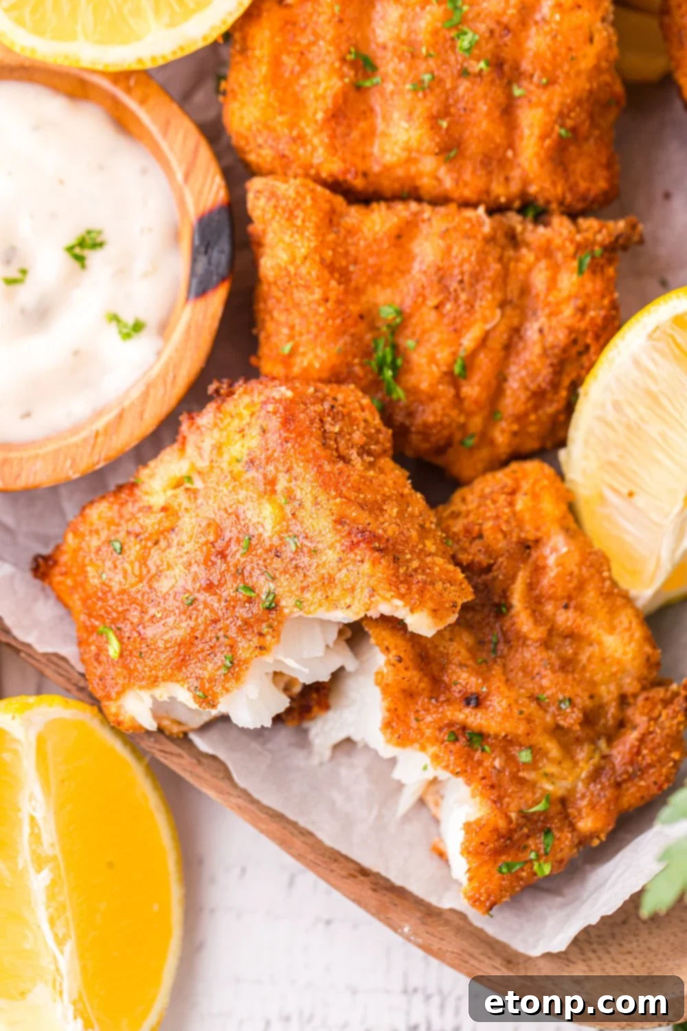 A piece of crispy air fryer fish broken in half, clearly showing the tender, flaky white fish interior contrasted with the golden, crunchy crust.