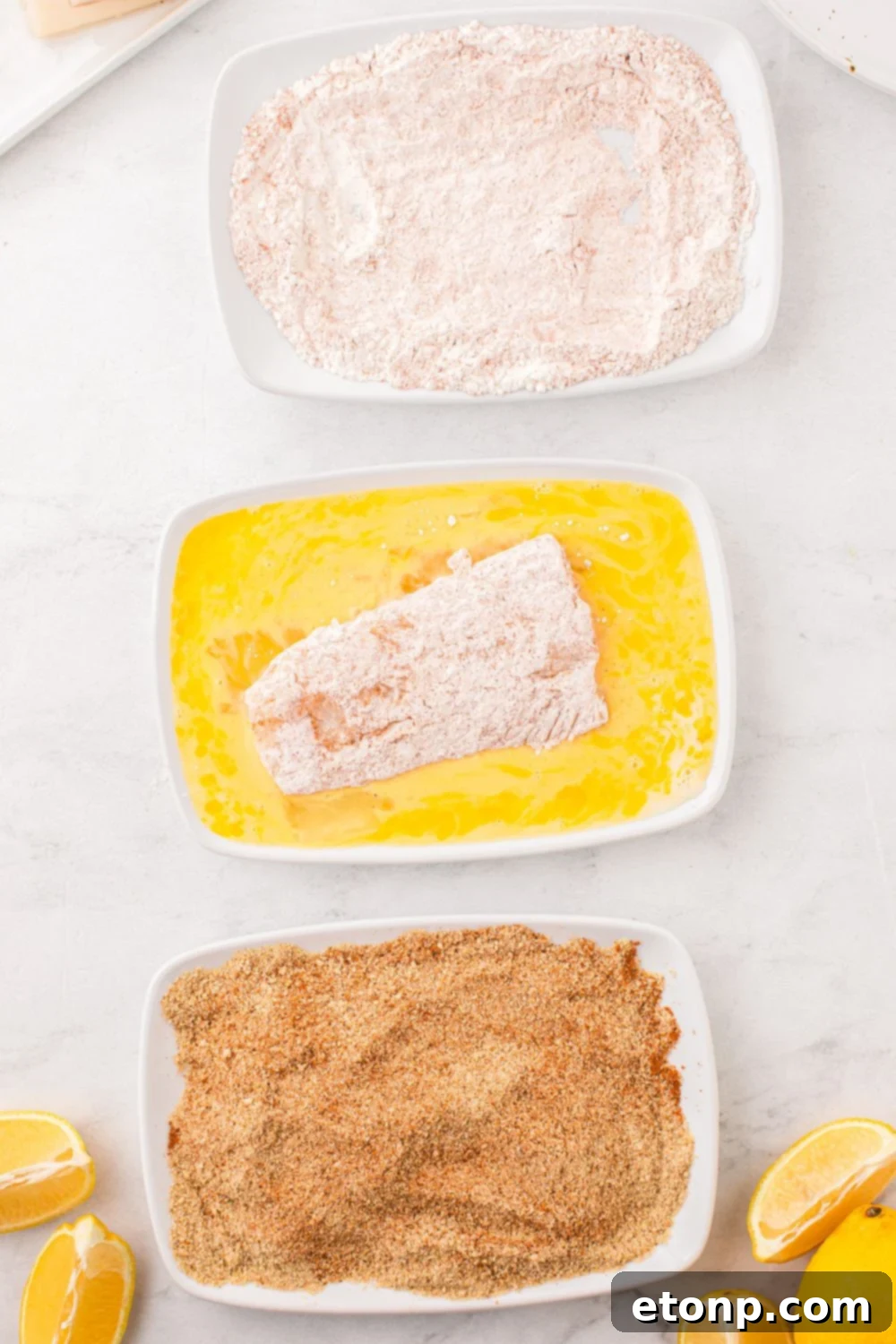 A fish fillet being dipped into a bowl of egg and buttermilk wash, creating a sticky layer for the breadcrumbs.