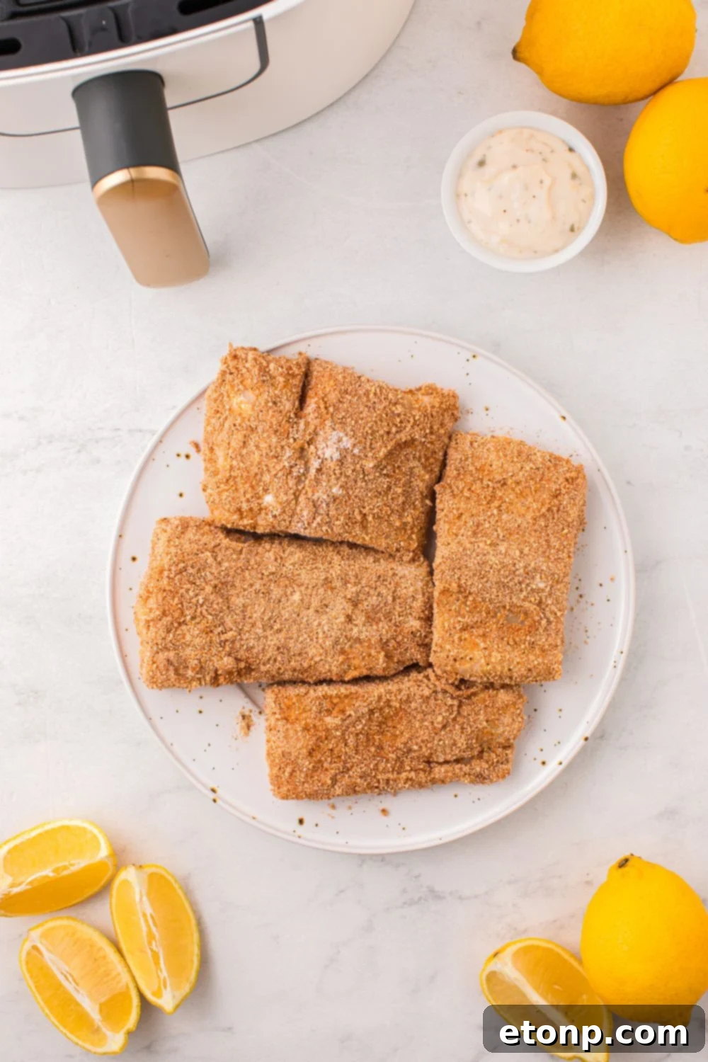 Several raw, breaded fish fillets neatly arranged on a plate next to an air fryer, ready for cooking.