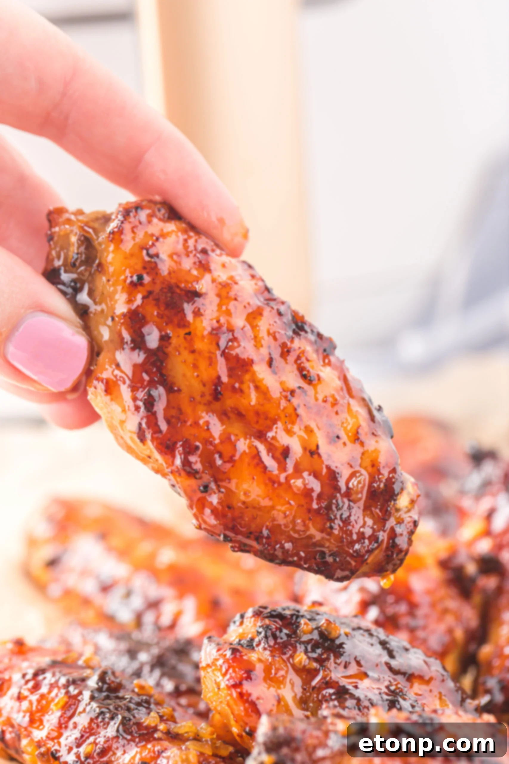 The Best Crispy Honey Garlic Air Fryer Chicken Wings 17 A hand holding up a single, perfectly glazed Air Fryer Honey Garlic Chicken Wing, showcasing its sticky, appetizing appearance.