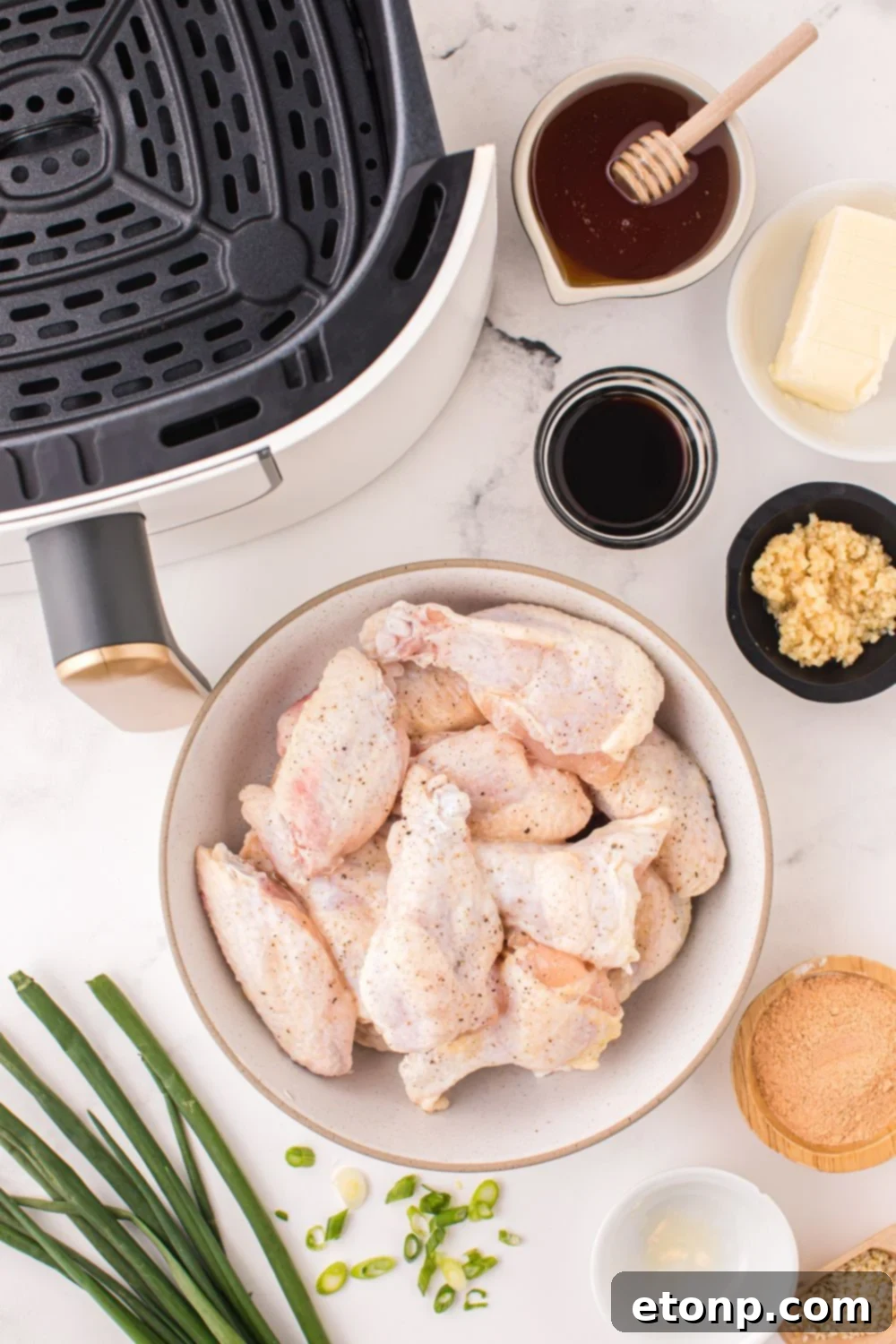 The Best Crispy Honey Garlic Air Fryer Chicken Wings 5 All the fresh ingredients for Air Fryer Honey Garlic Chicken Wings laid out on a table, including raw wings, butter, honey, soy sauce, and garlic, with an air fryer visible nearby.