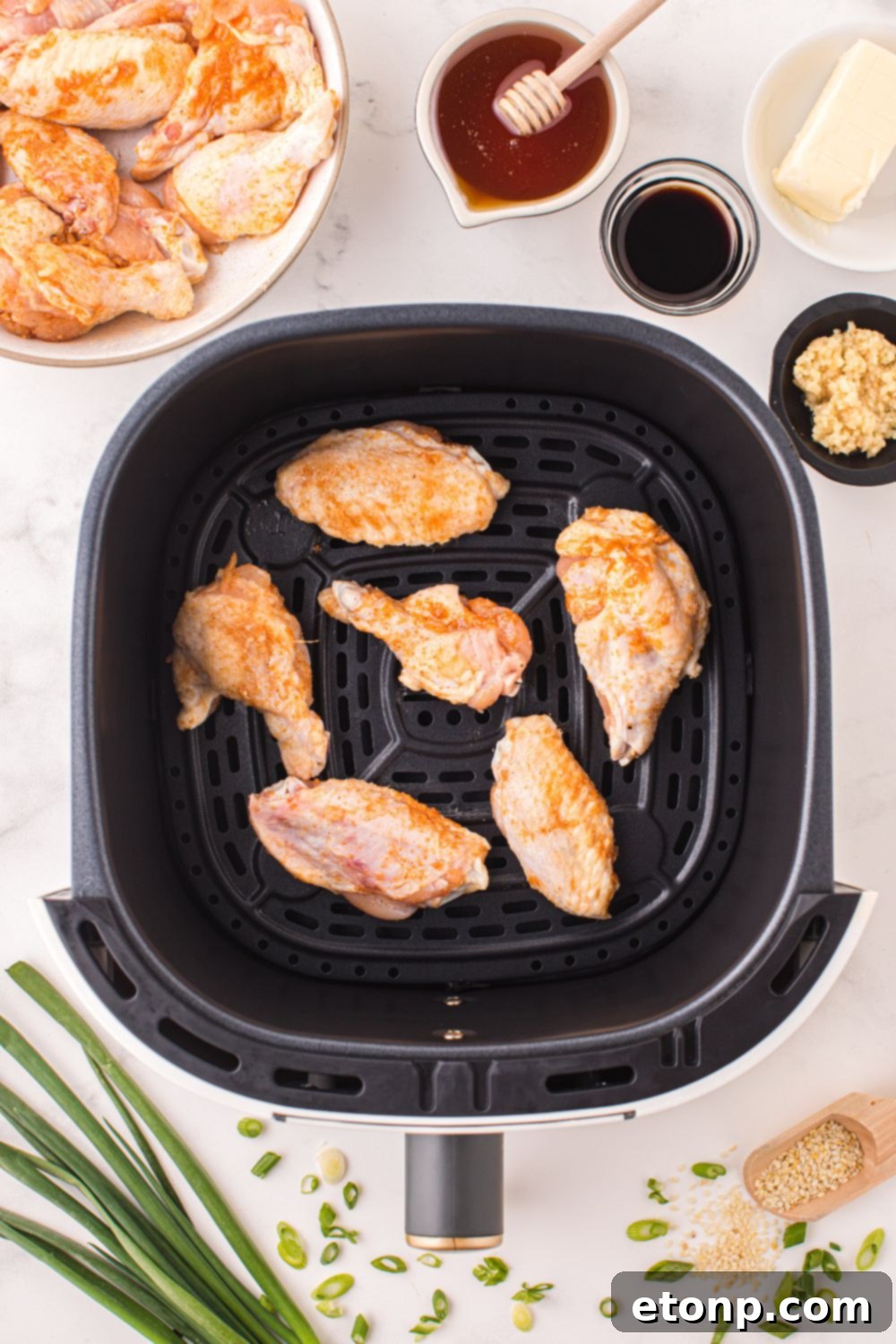 The Best Crispy Honey Garlic Air Fryer Chicken Wings 7 An air fryer basket filled with raw chicken wings, next to small bowls of honey, soy sauce, and minced garlic – key ingredients for the glaze.