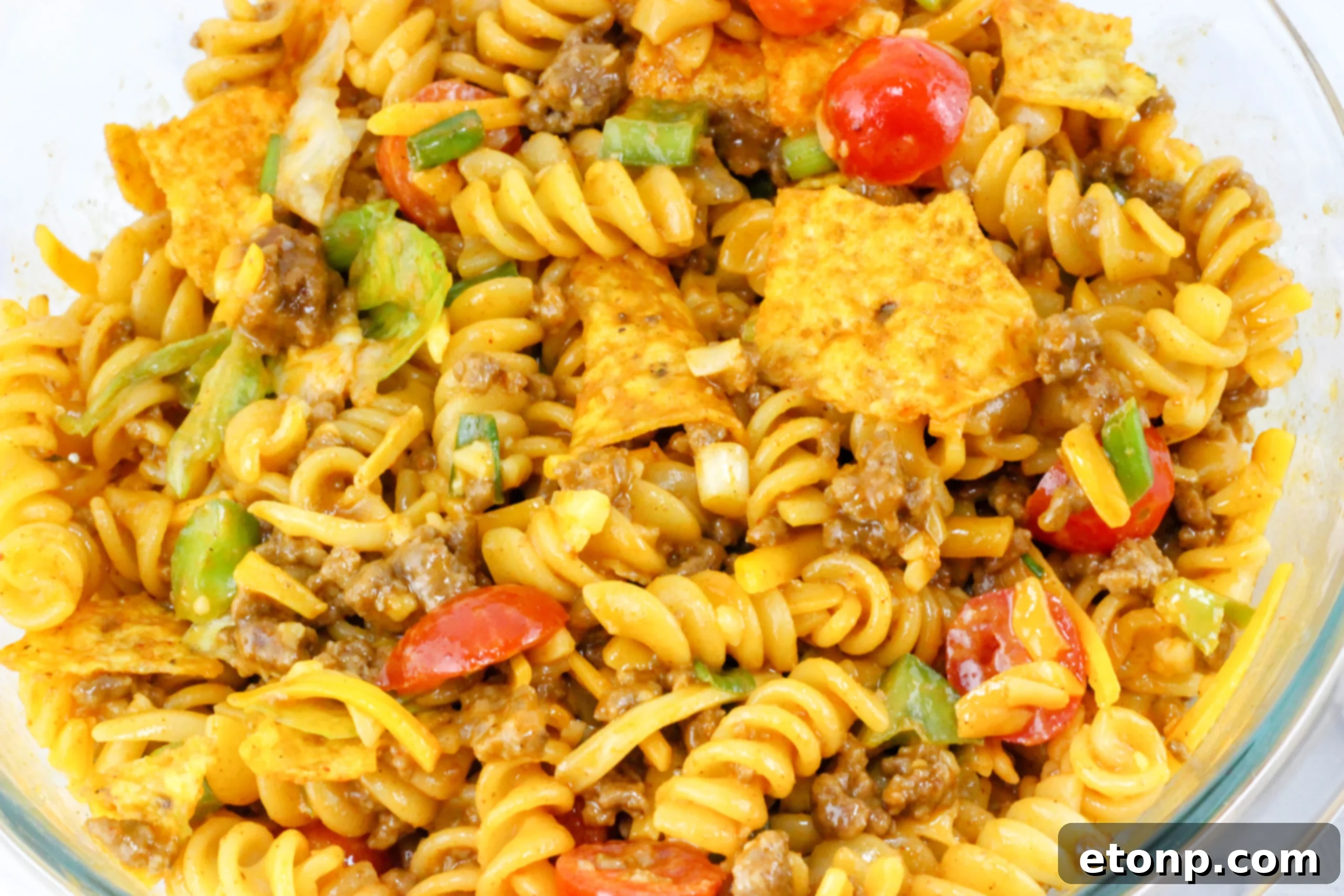 A vibrant bowl of Doritos Taco Pasta Salad, rich with colorful ingredients like ground beef, pasta, cheese, lettuce, and diced tomatoes, ready to be served at a gathering.