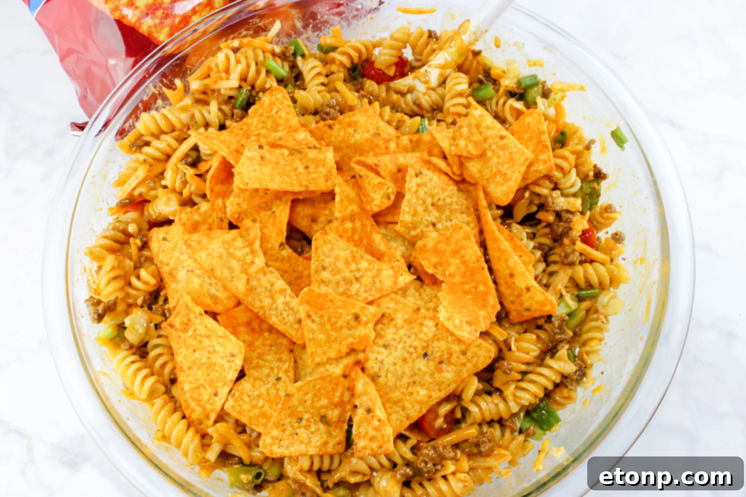 A large serving bowl filled with the prepared Doritos Taco Pasta Salad, garnished with fresh green onions and a dollop of sour cream, making it an inviting centerpiece.