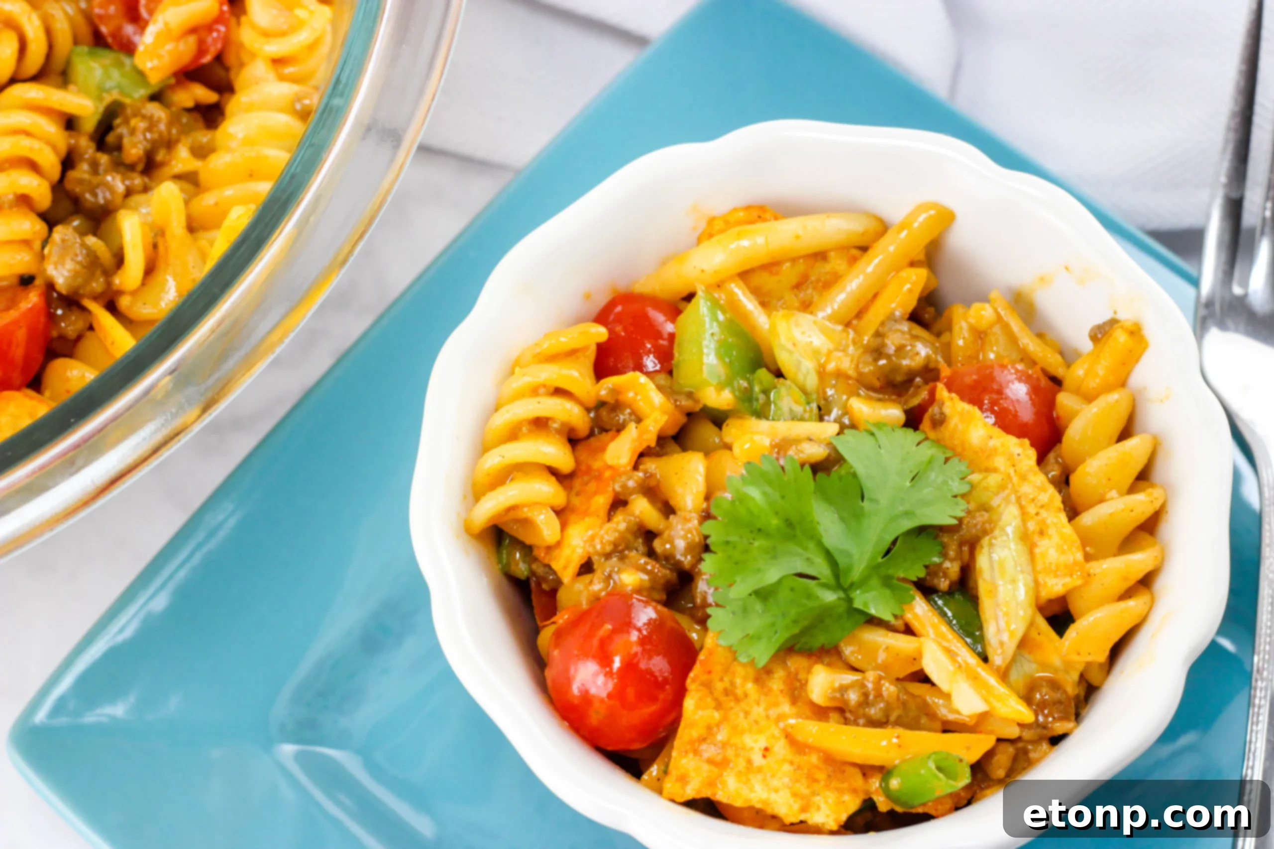 Two hands holding forks, poised above a bowl of Doritos Taco Pasta Salad, illustrating the immediate desire to dig in.