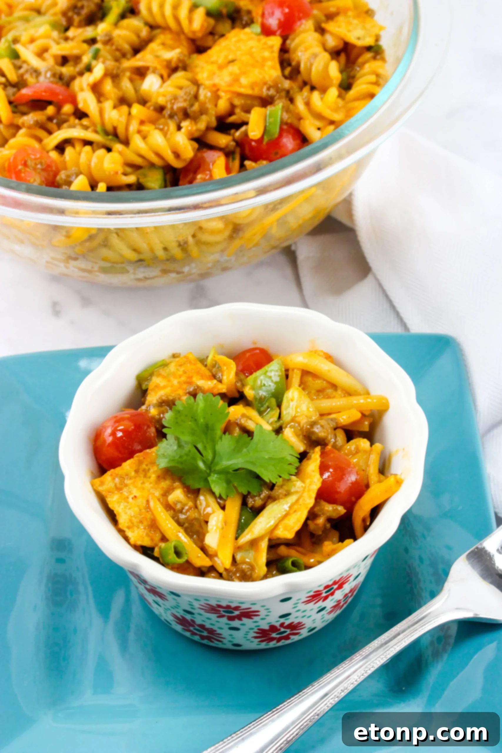 A close-up of the Doritos Taco Pasta Salad, highlighting the textures of the shredded cheese, diced green bell peppers, and the seasoned ground beef amidst the pasta.