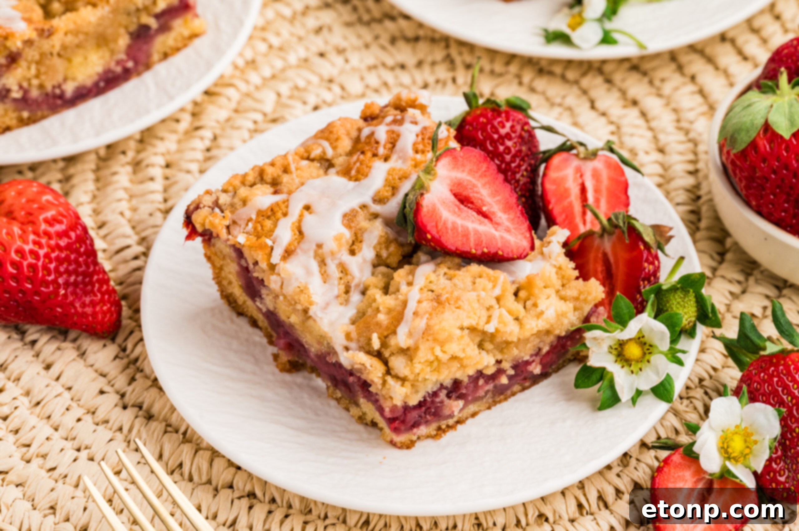 Fresh Strawberry Coffee Cake 11 An inviting overhead shot of a Strawberry Coffee Cake on a white plate, surrounded by scattered fresh strawberry slices, emphasizing its vibrant appeal.