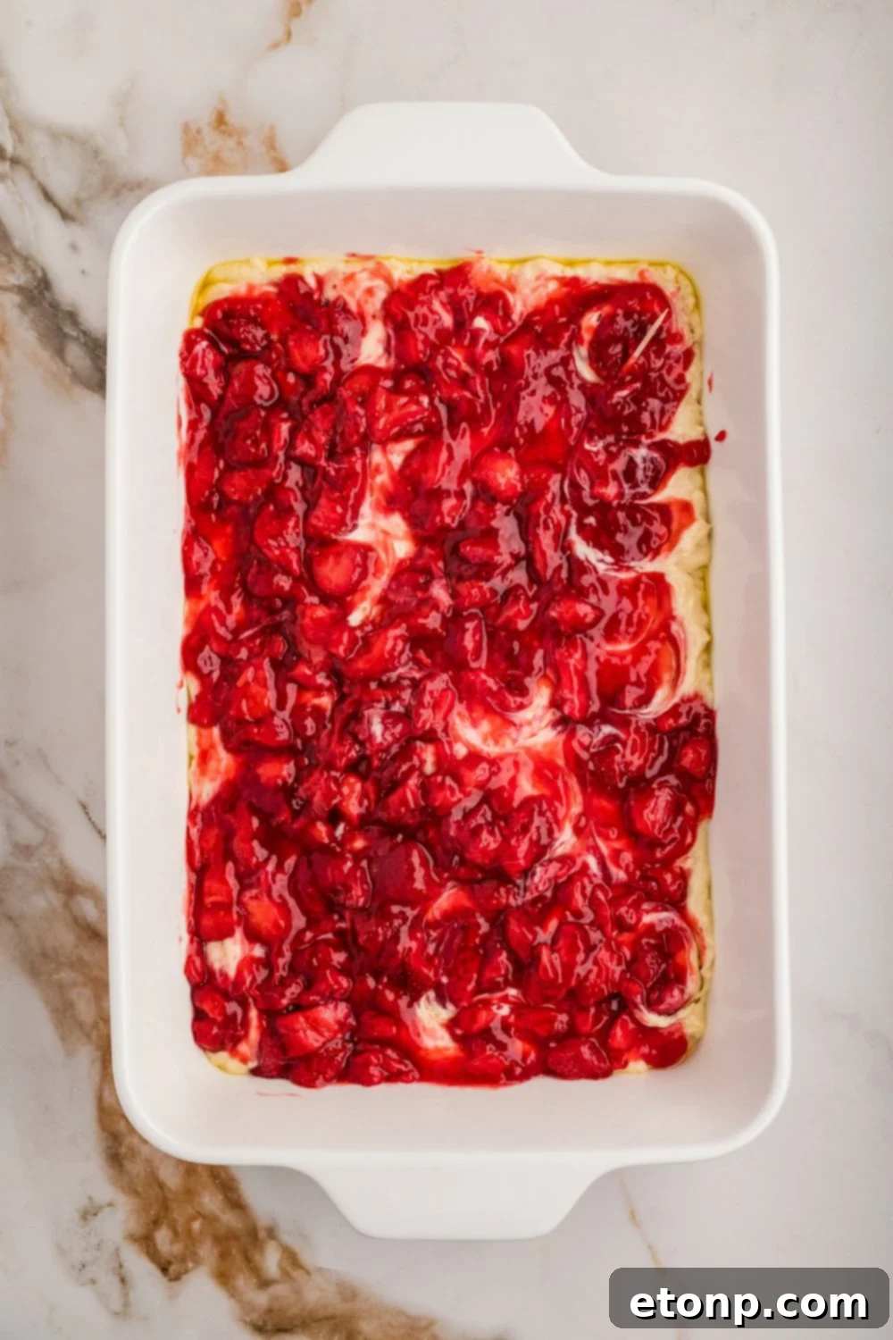 Fresh Strawberry Coffee Cake 18 A layer of bright red fruit topping, possibly strawberry, spread over raw cake batter in a baking dish, creating a vibrant swirl effect.