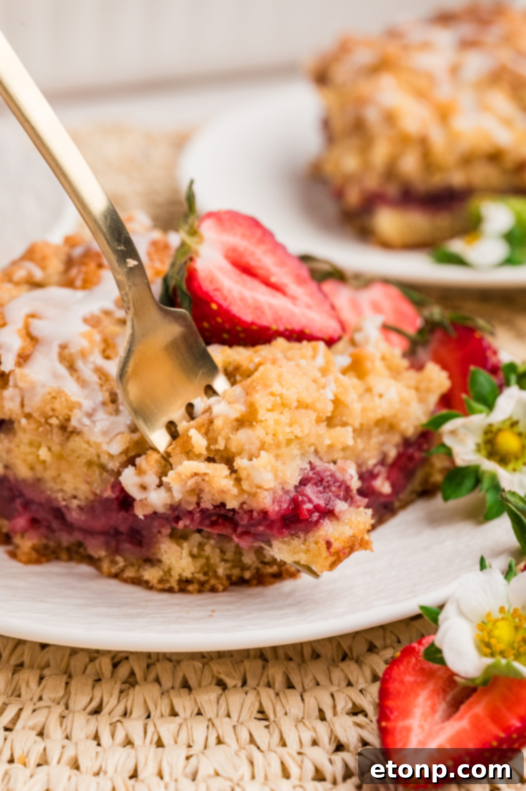 Fresh Strawberry Coffee Cake 22 A white plate holding a slice of Strawberry Coffee Cake, garnished with fresh strawberries, with a fork poised to take a bite, highlighting its soft texture.
