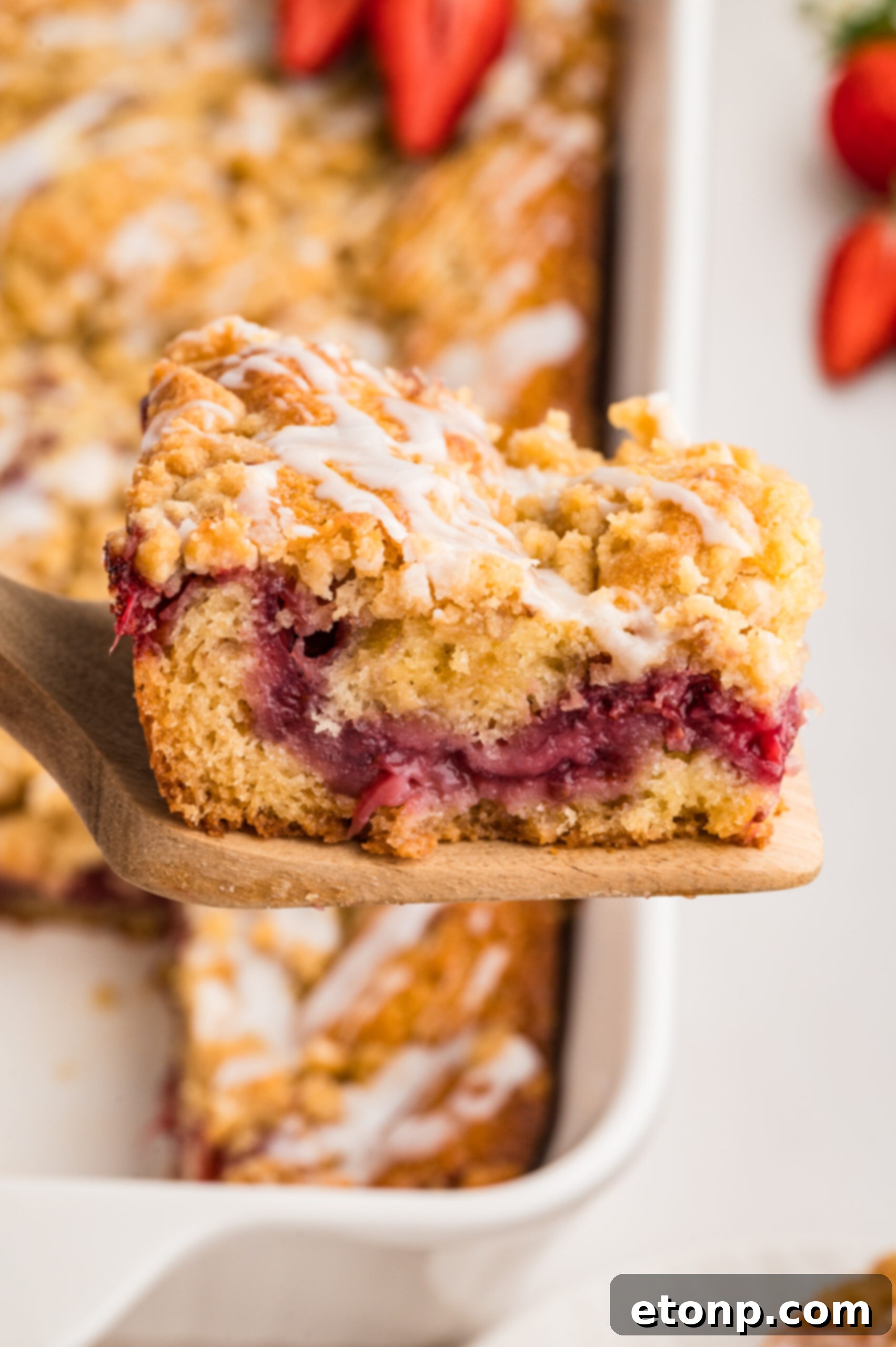 Fresh Strawberry Coffee Cake 4 A generous slice of freshly baked Strawberry Coffee Cake being carefully lifted from the pan with a wooden spatula, showing its moist interior and fruit swirls.