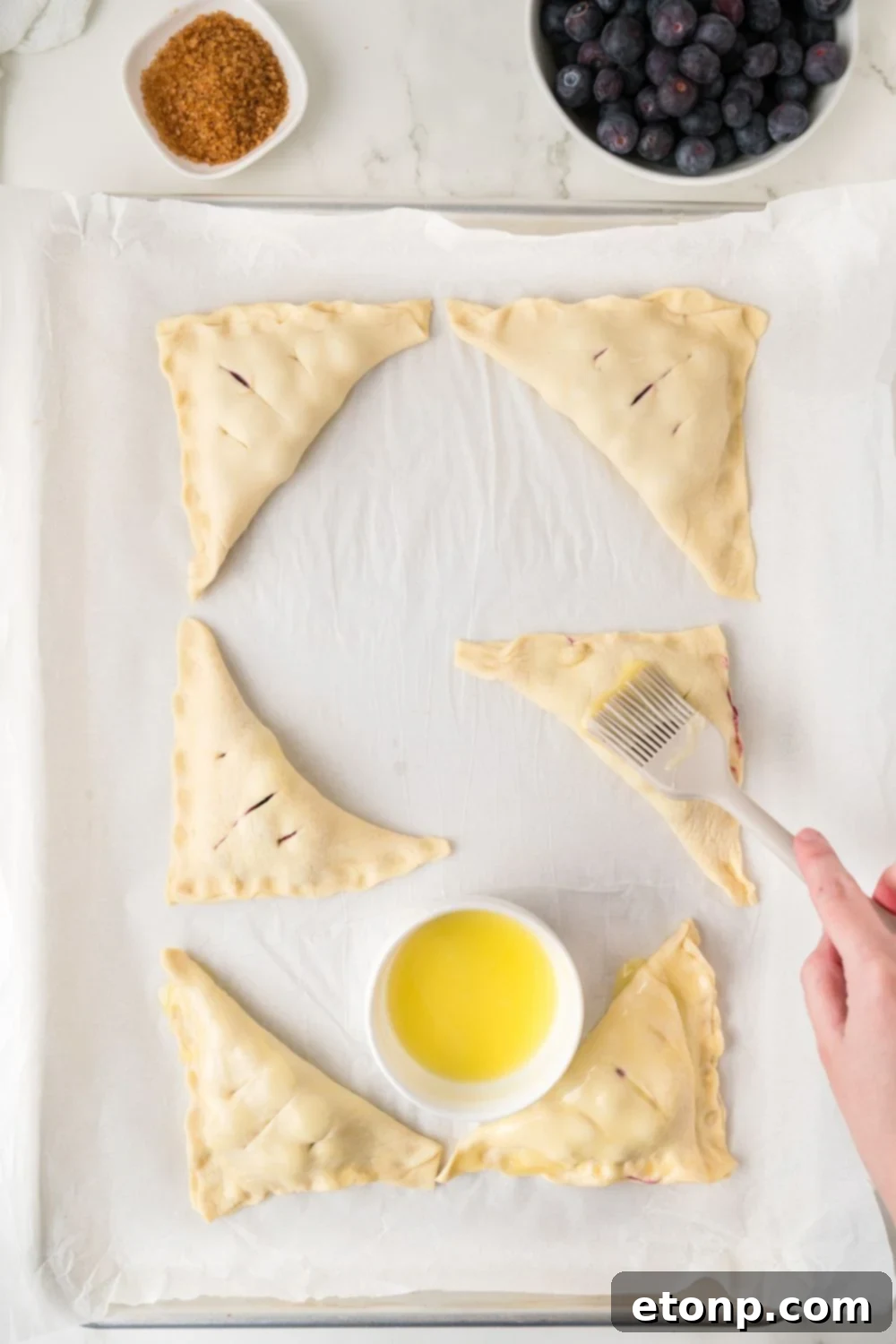 poking holes in pastry and a small bowl of butter to the side for Blueberry Turnovers