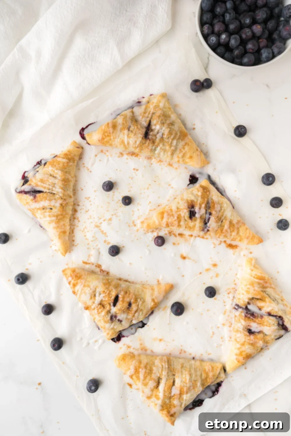 overhead view of Blueberry Turnovers on baking tray with a drizzle of glaze on top 