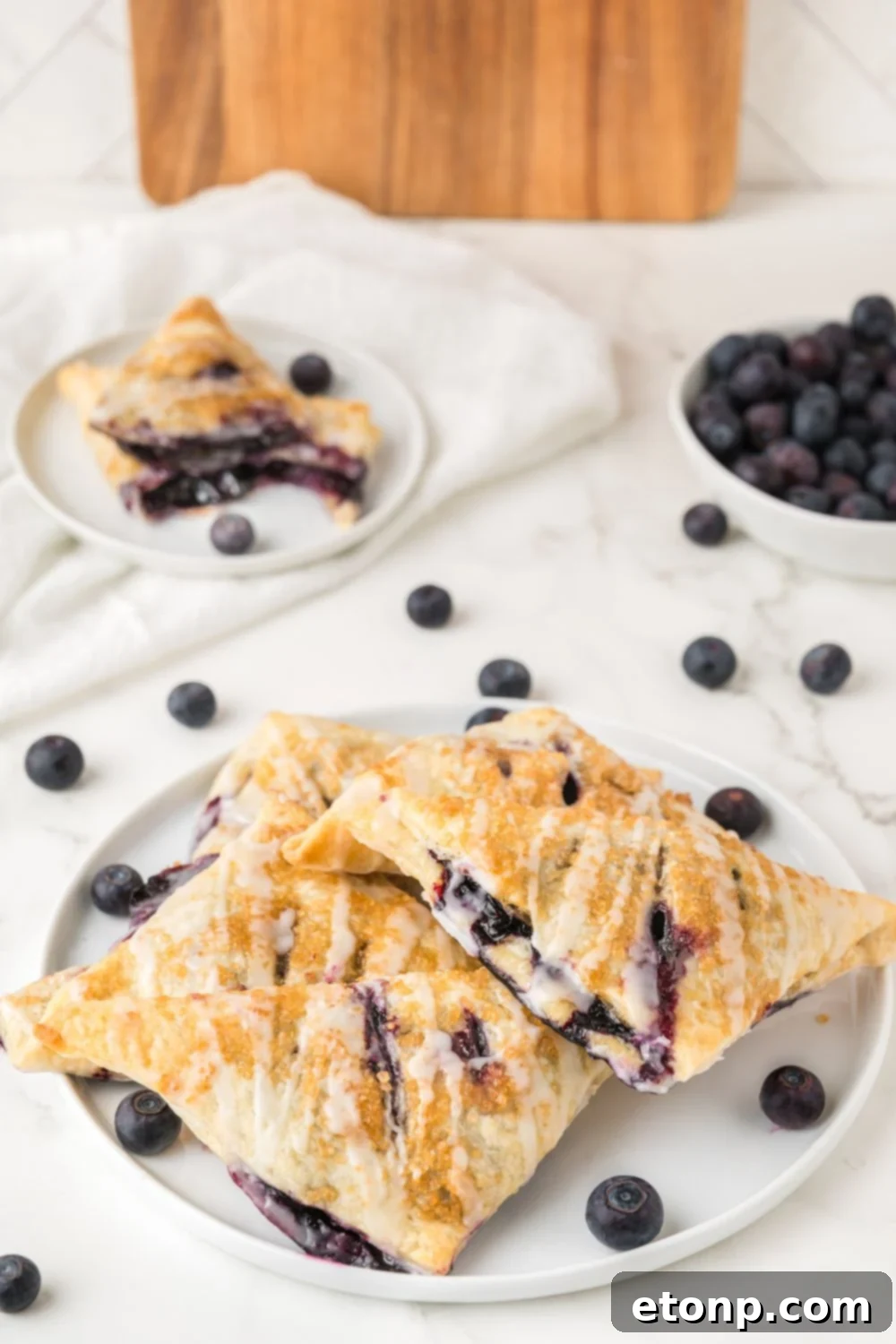 Blueberry Turnovers on a plate with fresh blueberries in a bowl and around the table 