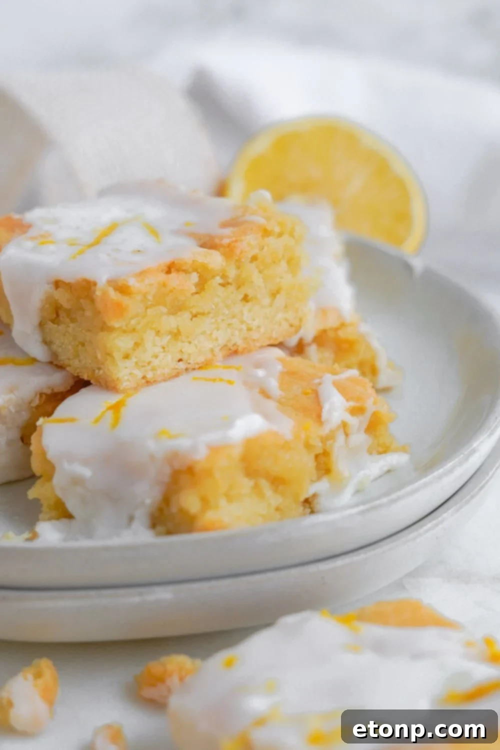 Lemon Sugar Cookie Bars stacked on a platter and a lemon sliced in half sitting on table to the side of bowl 