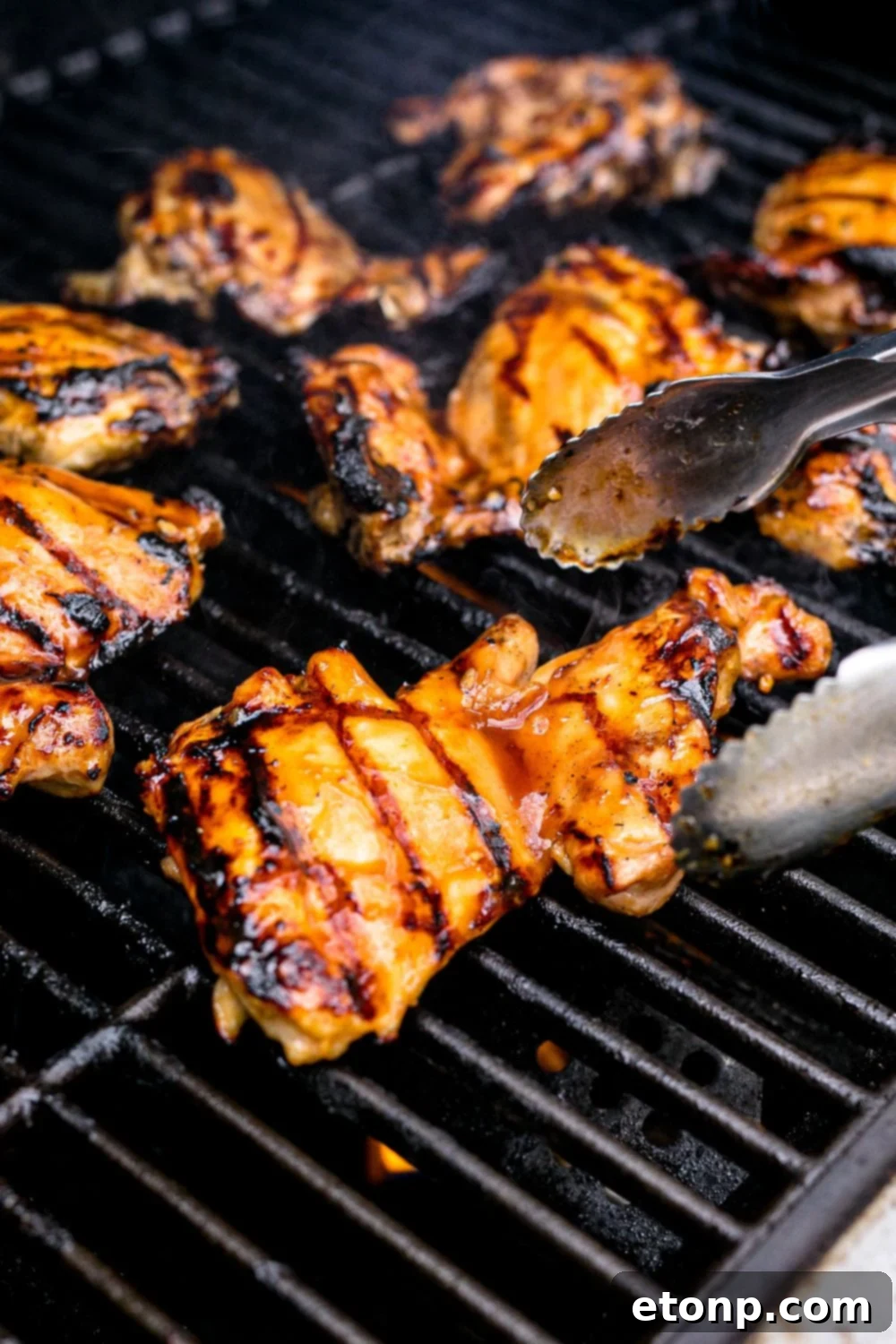 Succulent Huli Huli chicken cooking on a hot grill with tongs poised to turn the pieces for even cooking