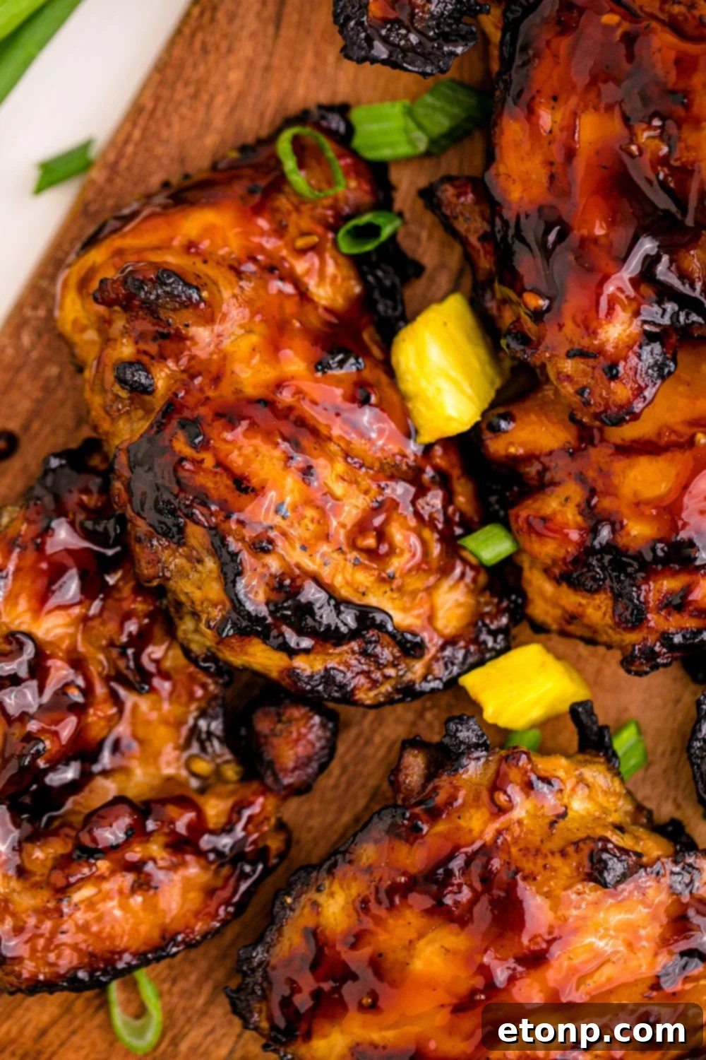 Expertly grilled Huli Huli chicken slices arranged on a rustic wooden cutting board, highlighting the perfect char and glaze