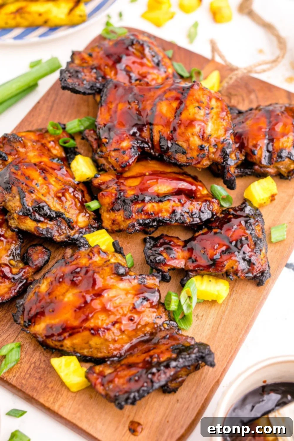 A generous platter of Huli Huli Chicken garnished with green onions and a small bowl of extra glaze on a table