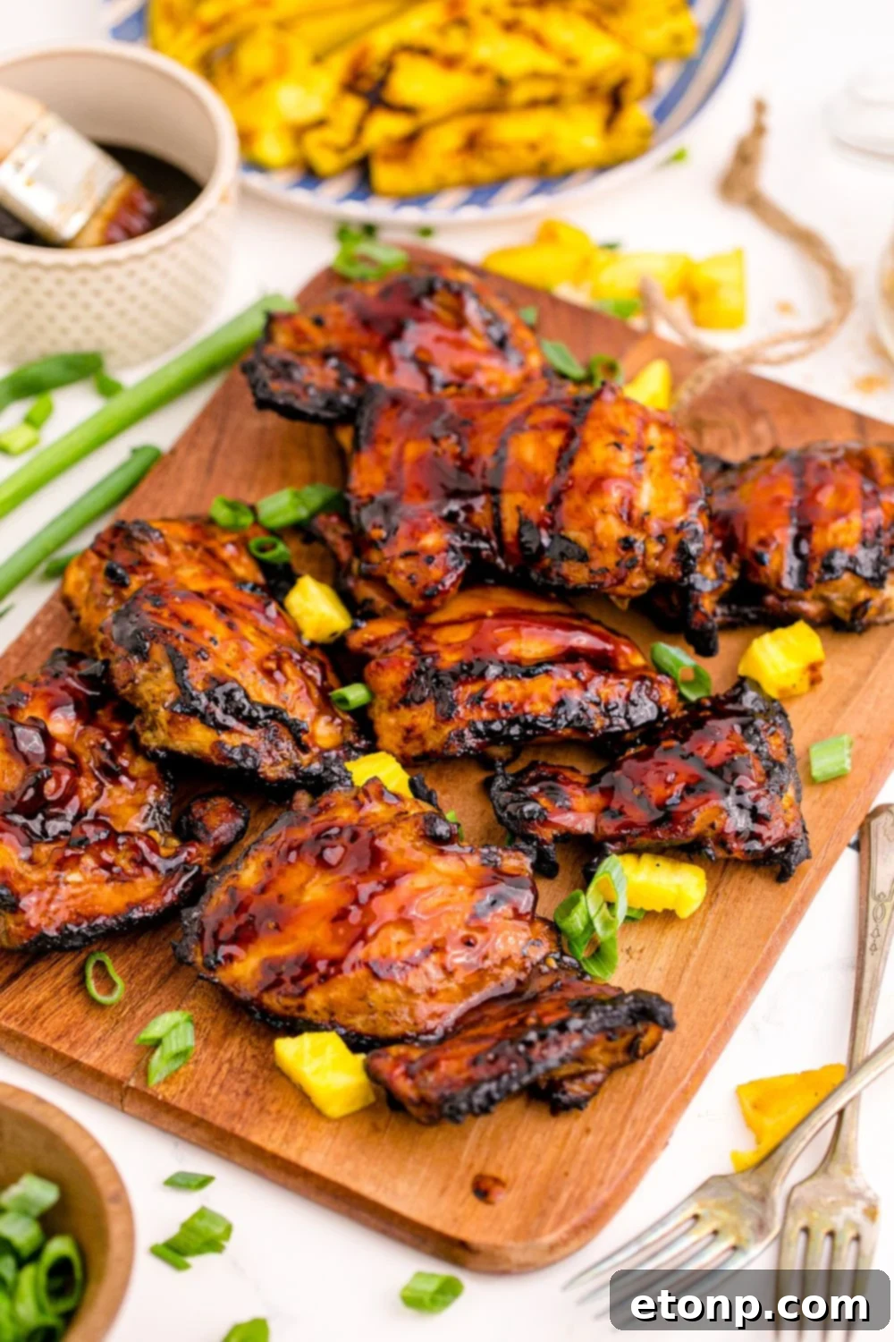 A serving bowl of Huli Huli Chicken garnished with vibrant green onions, with fresh pineapple slices on the side