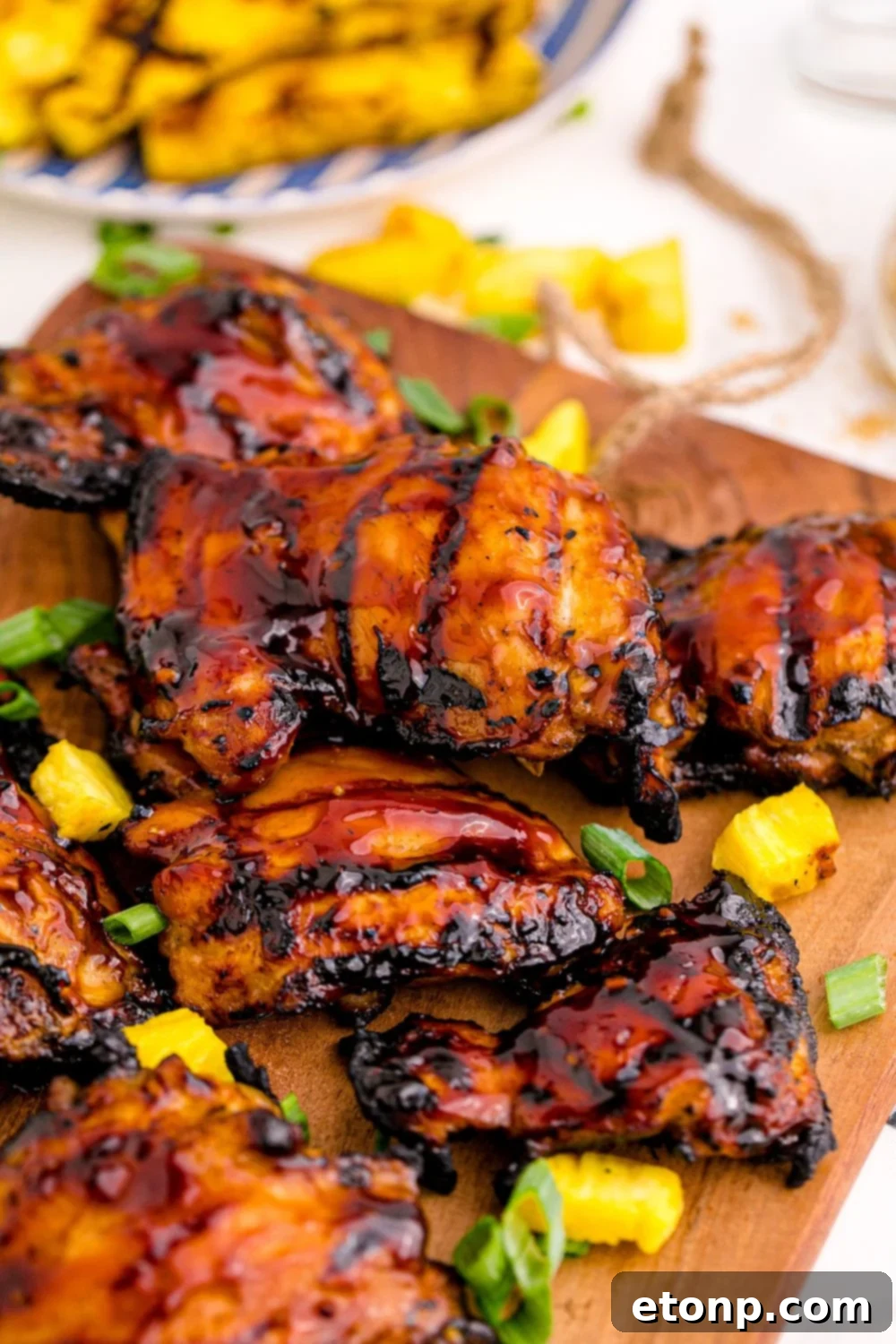 Perfectly grilled Hawaiian Huli Huli chicken on a wooden cutting board with caramelized grilled pineapple on a white plate