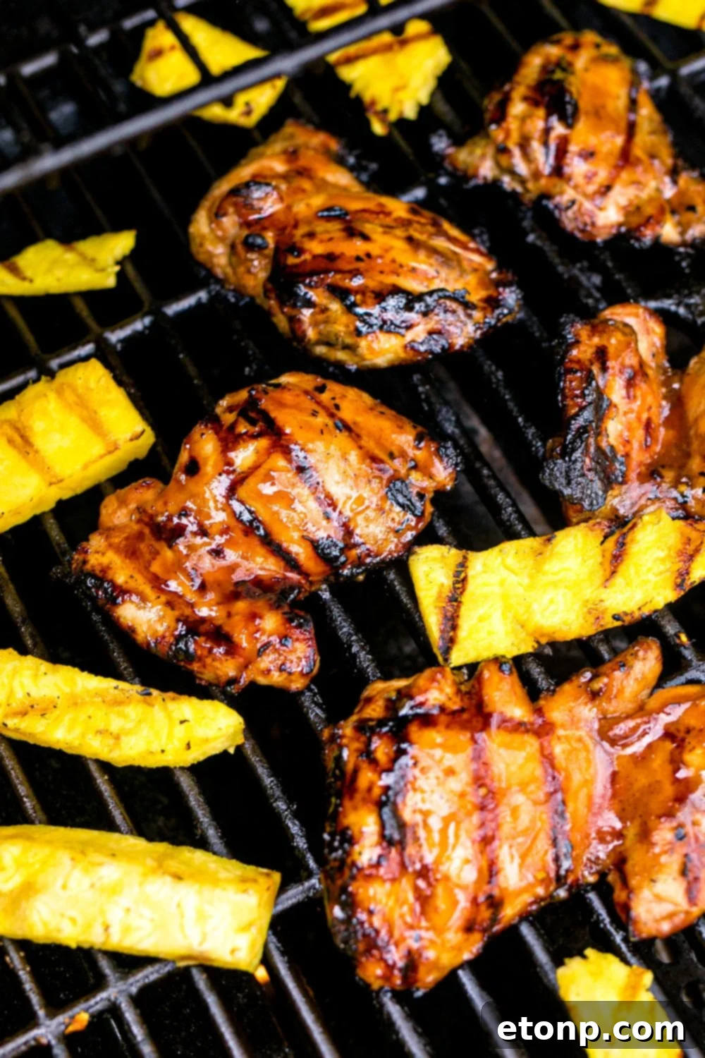 Huli Huli Chicken cooking on a grill alongside fresh pineapple slices, creating a tropical aroma