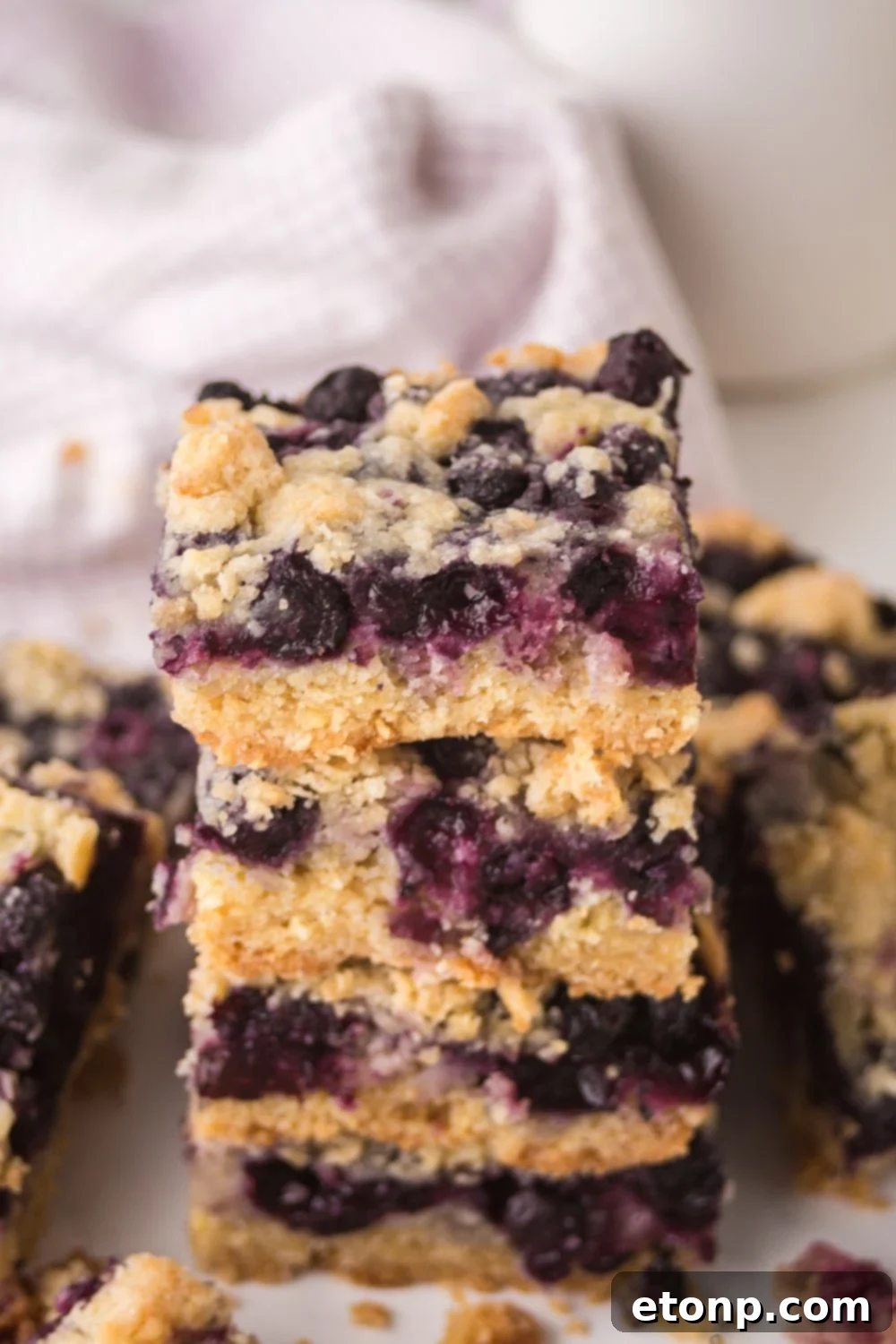 Blueberry Crumb Bars stacked on top of one another on table with more bars spread out around the table 