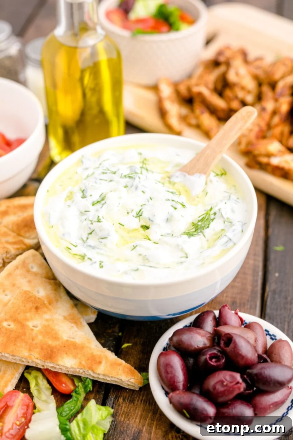 Tzatziki Sauce in a ceramic bowl with pita bread, olives and more around the bowl for dipping 