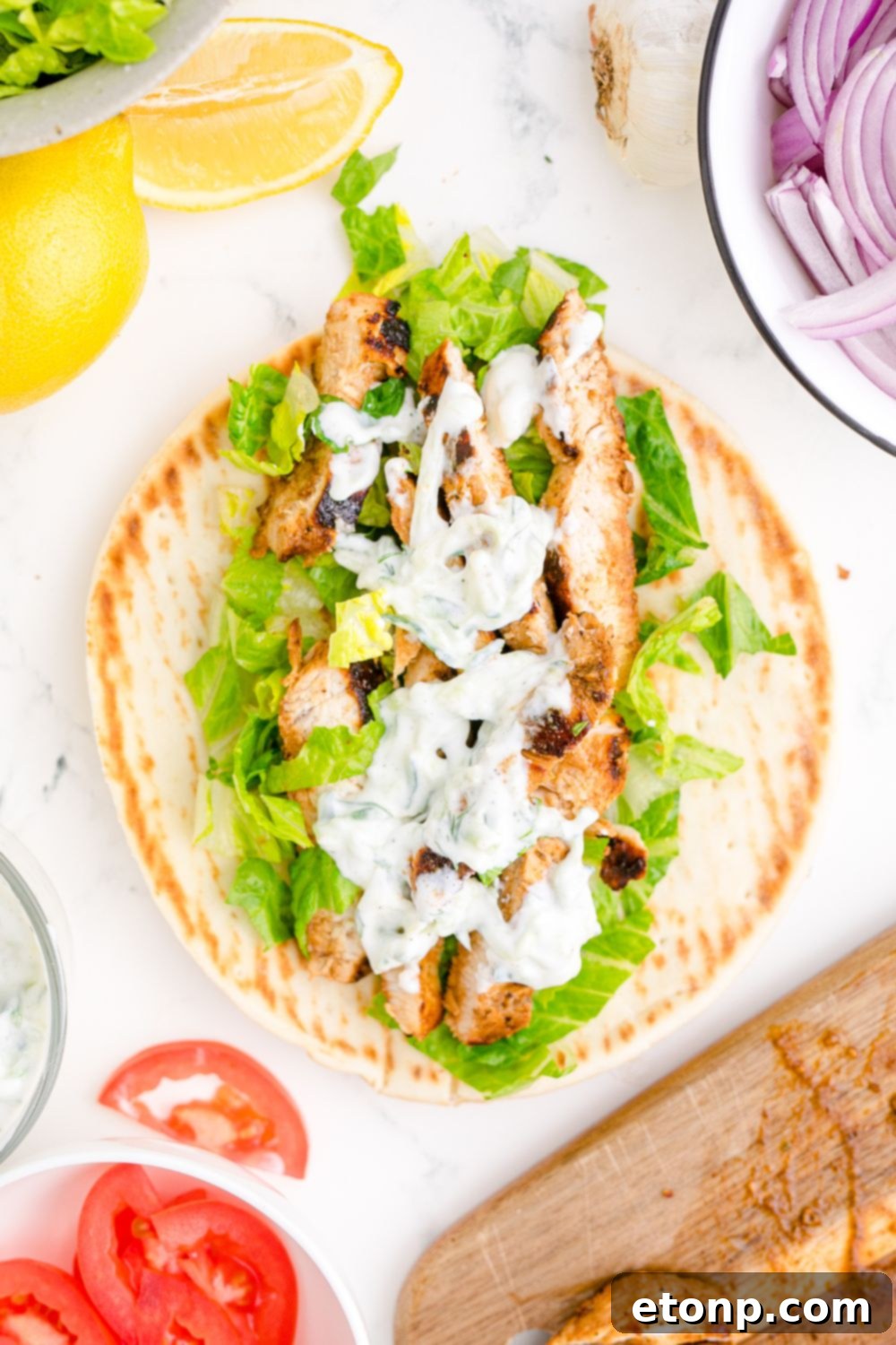 Tzatziki Sauce on a gyro on table with sliced tomatoes and onions to the side 